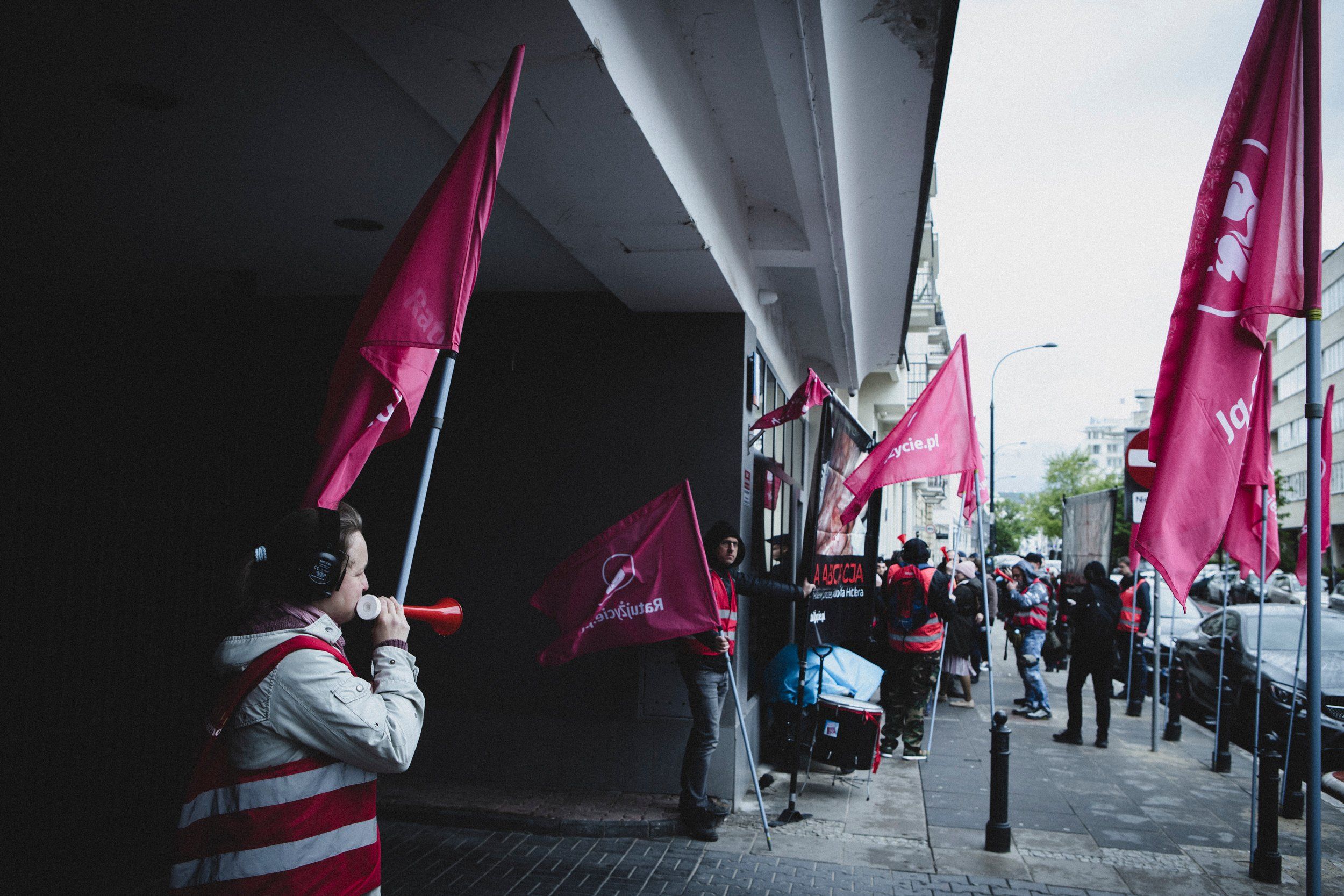 Kolejny raz pod przychodnią Abotak przeciwnicy aborcji zorganizowali swoje zgromadzenie. Przez wiele godzin uzbrojeni w wuwuzele, głośne nagranie płaczu dziecka utrudniają pracę przychodni, życie mieszkańców oraz zwykłe przejście przez chodnik przypadkowym przechodniom.
Dzisiaj kilka razy doszło do agresji słownej i naruszania nietykalności cielesnej, zwłaszcza ze strony jednej uczestniczki zgromadzenia, w stosunku do przechodniów oraz osób dokumentujących całe zajście. Byliśmy wulgarnie wyzywani, wypychani i kopani, w tym ja, co finalnie będzie skutkowało zgłoszeniem tego na policji.
Przeciwnicy aborcji regularnie trąbią prosto w ucho osobom, które chcą wejść do przychodni. Co ciekawe sami noszą słuchawki chroniące przed hałasem.
Osoby pracujące w Abotak dostały dzisiaj wsparcie miedzy innymi  od Polskie Babcie, Strajk Kobiet, Wschód oraz przyjaciół i przyjaciółek, które stały z transparentami i plakatami po drugiej stronie ulicy lub bezpośrednio pod drzwiami przychodni.