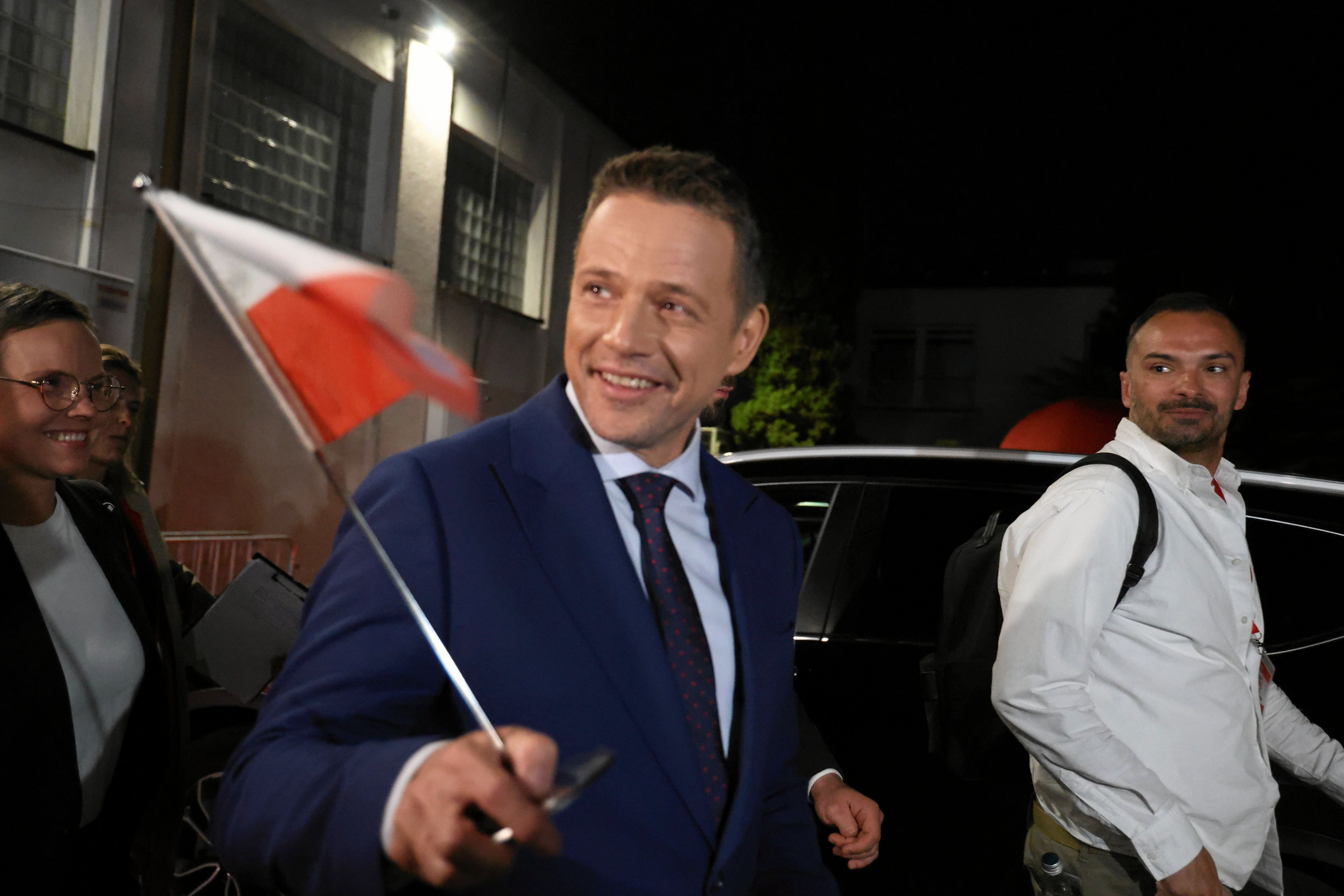 Uśmiechnięty mężczyzna w ciemnym garniturze z flagą biało-czerwoną