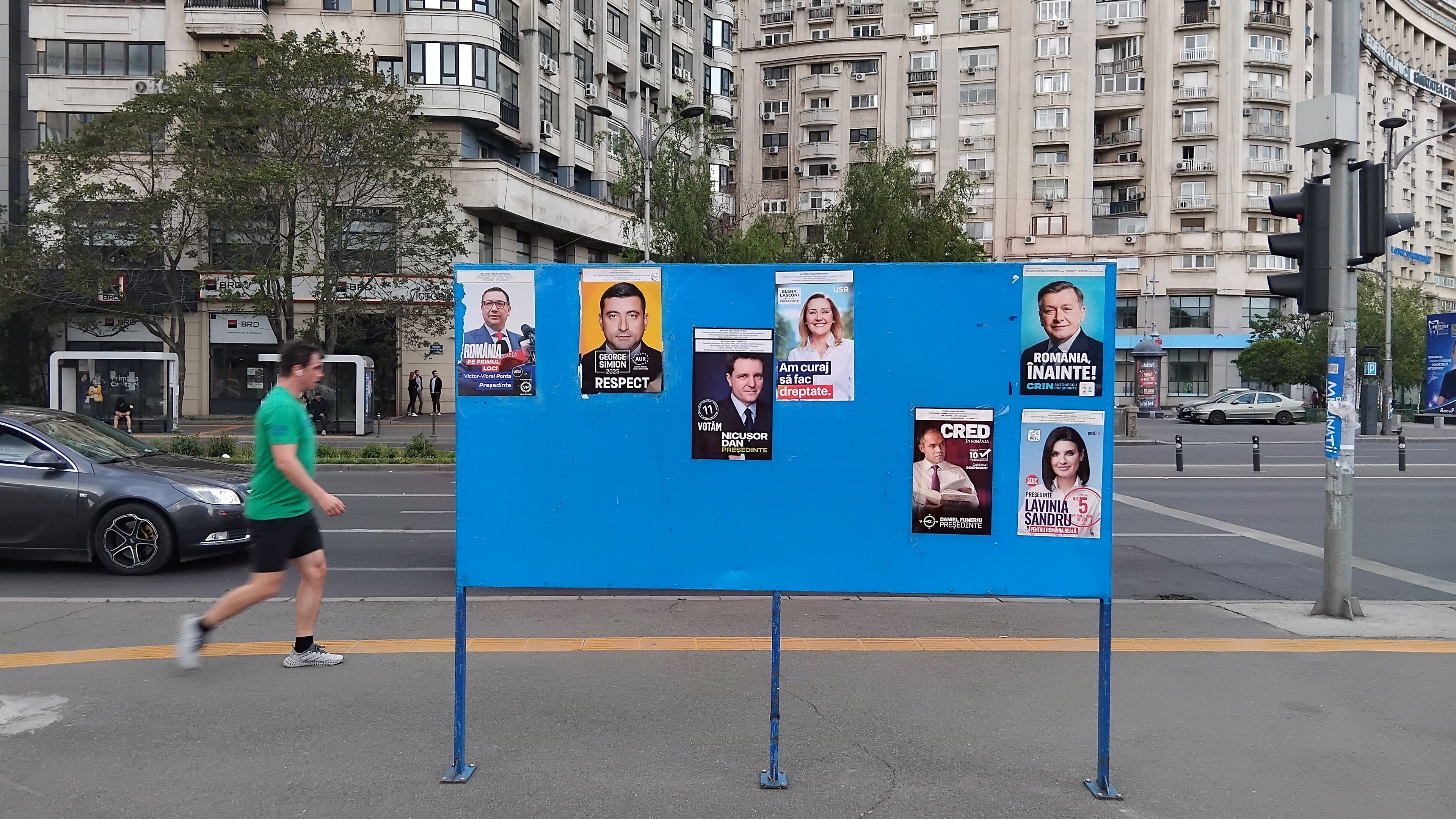 Rumuński kodeks wyborczy nie pozwala na wielkoformatową reklamę kandydatów politycznych. Dopuszczalne jest tylko rozwieszanie prostych, informacyjnych plakatów wyborczych z portretem osoby kandydującej, jego/jej imieniem i nazwiskiem oraz hasłem wyborczym. Tu taki plakat widoczny przy placu Zwycięstwa w Bukareszcie, 2 maj 2025.