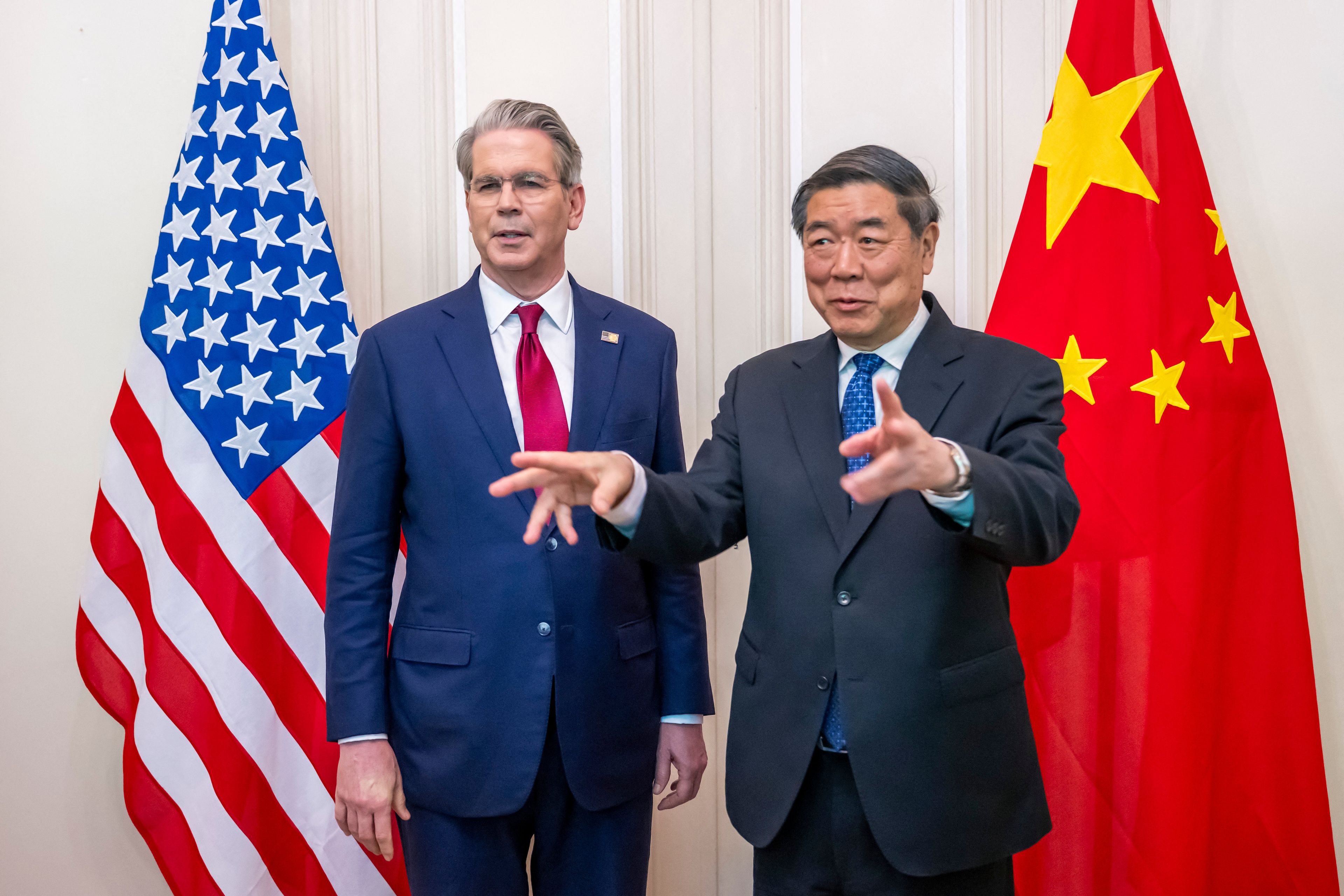 Dwóch mężczyzn w garniturach, amerykański sekretarz skarbu Scott Bessent i chiński wicepremier He Lifeng na tle flag USA i Chin