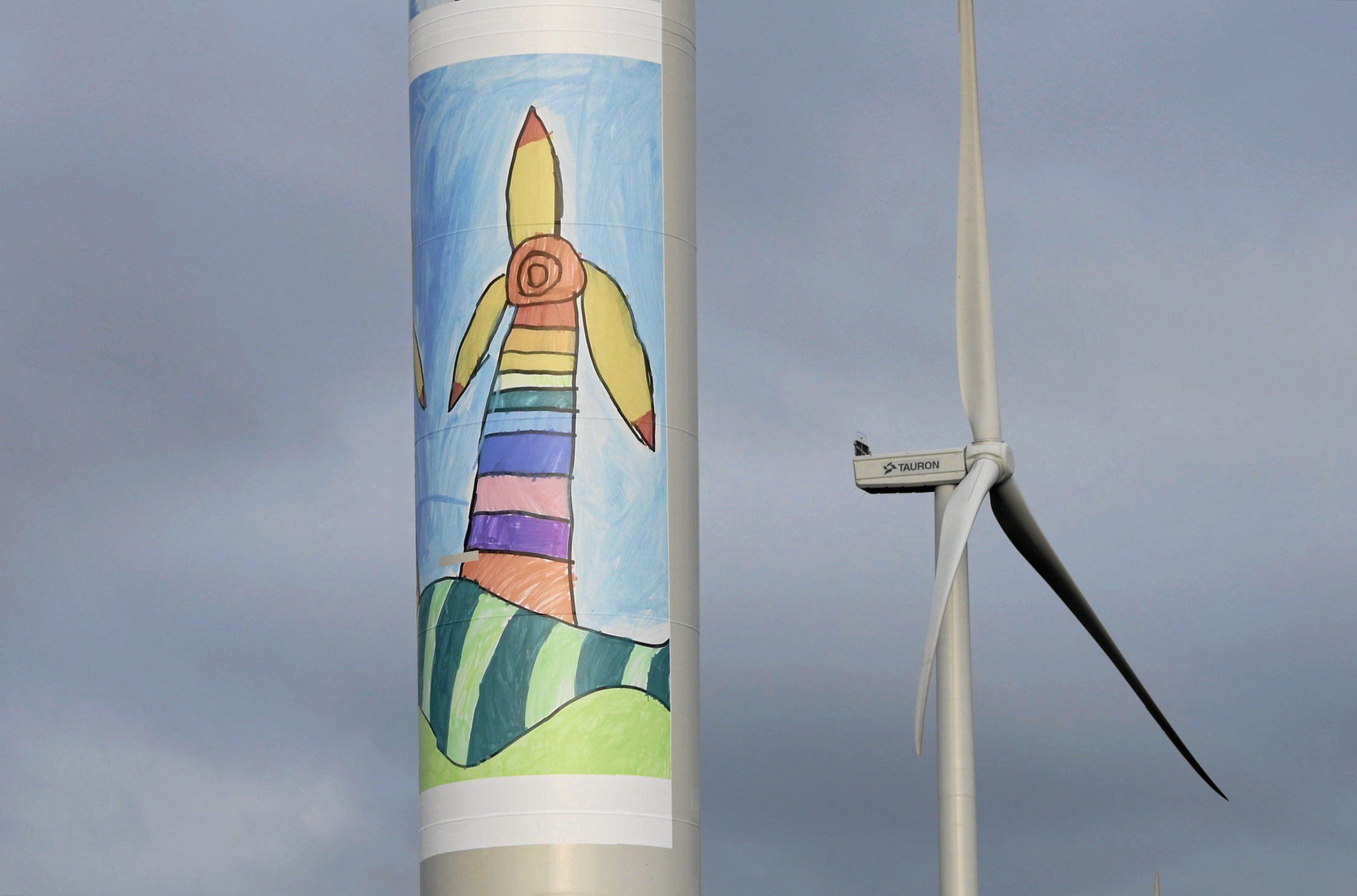 Farma wiatrowa, dwa wiatraki - na podstawie pierwszego bliższego, mural udający dziecięcy rysunek wiatraka