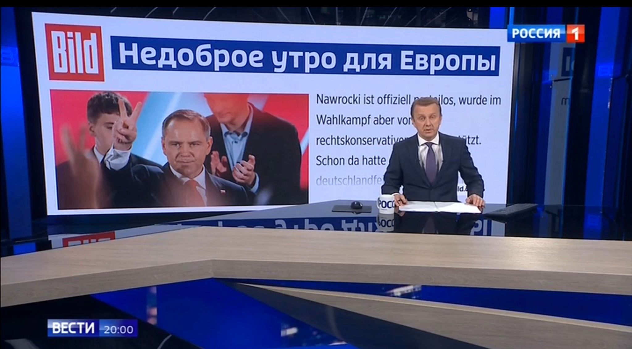 Prezenter w studio. Za nim zdjęcie Karola Nawrockiego i rosyjski napis