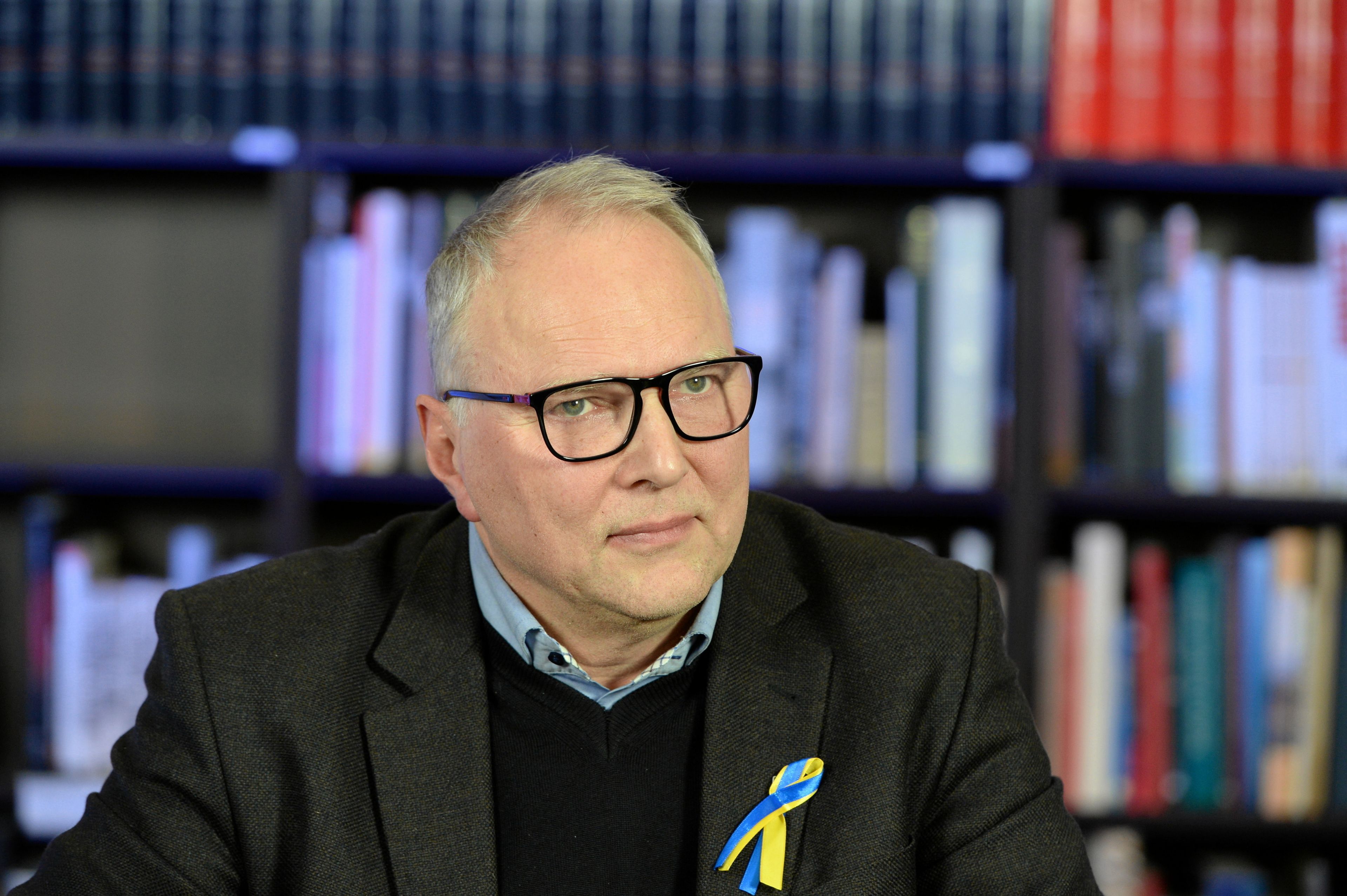 Mężczyzna w okularach, w średnim wieku, na tle regału z książkami