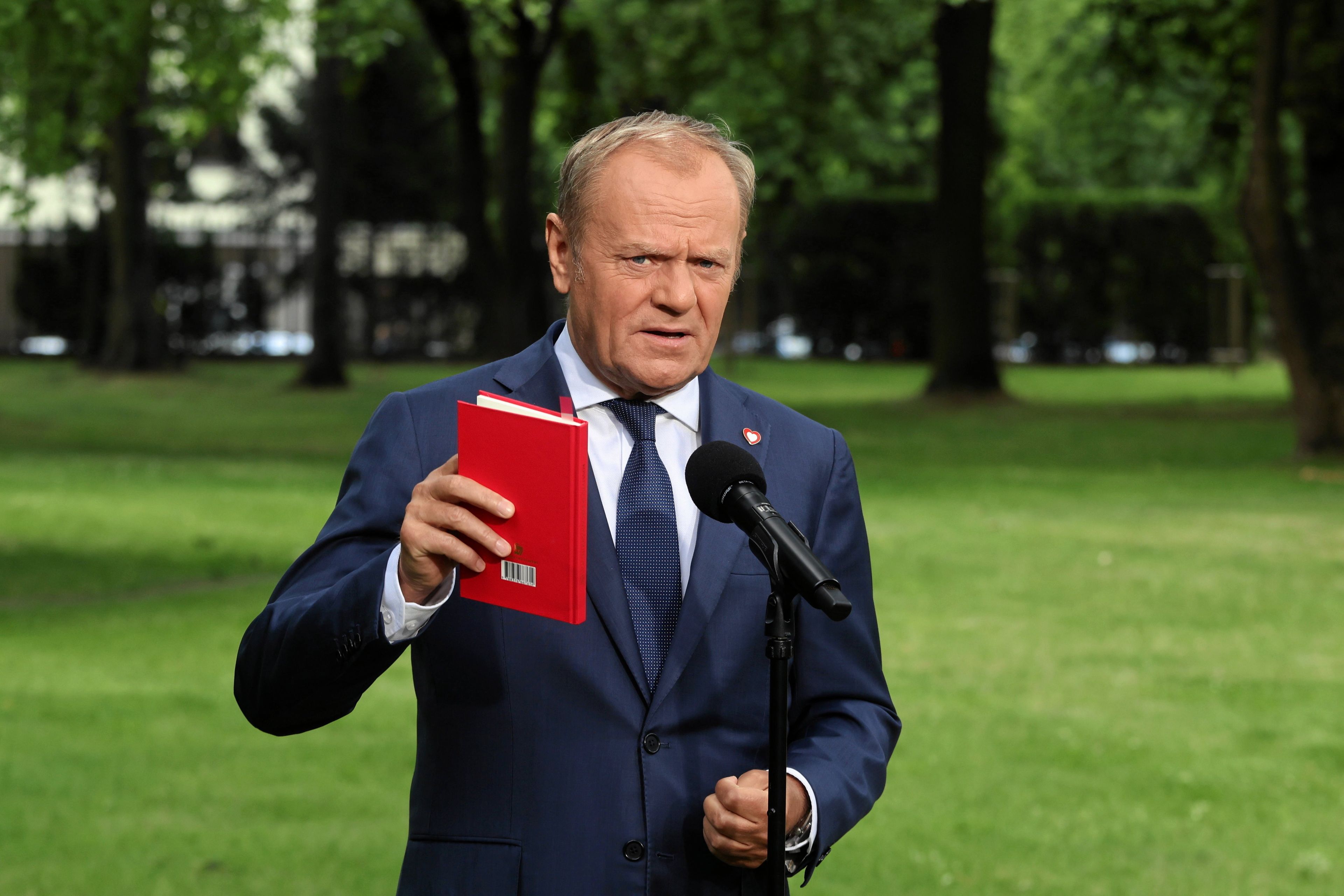 Premier Donald Tusk z Konstytucją w czerwonej okładce w prawej dłoni