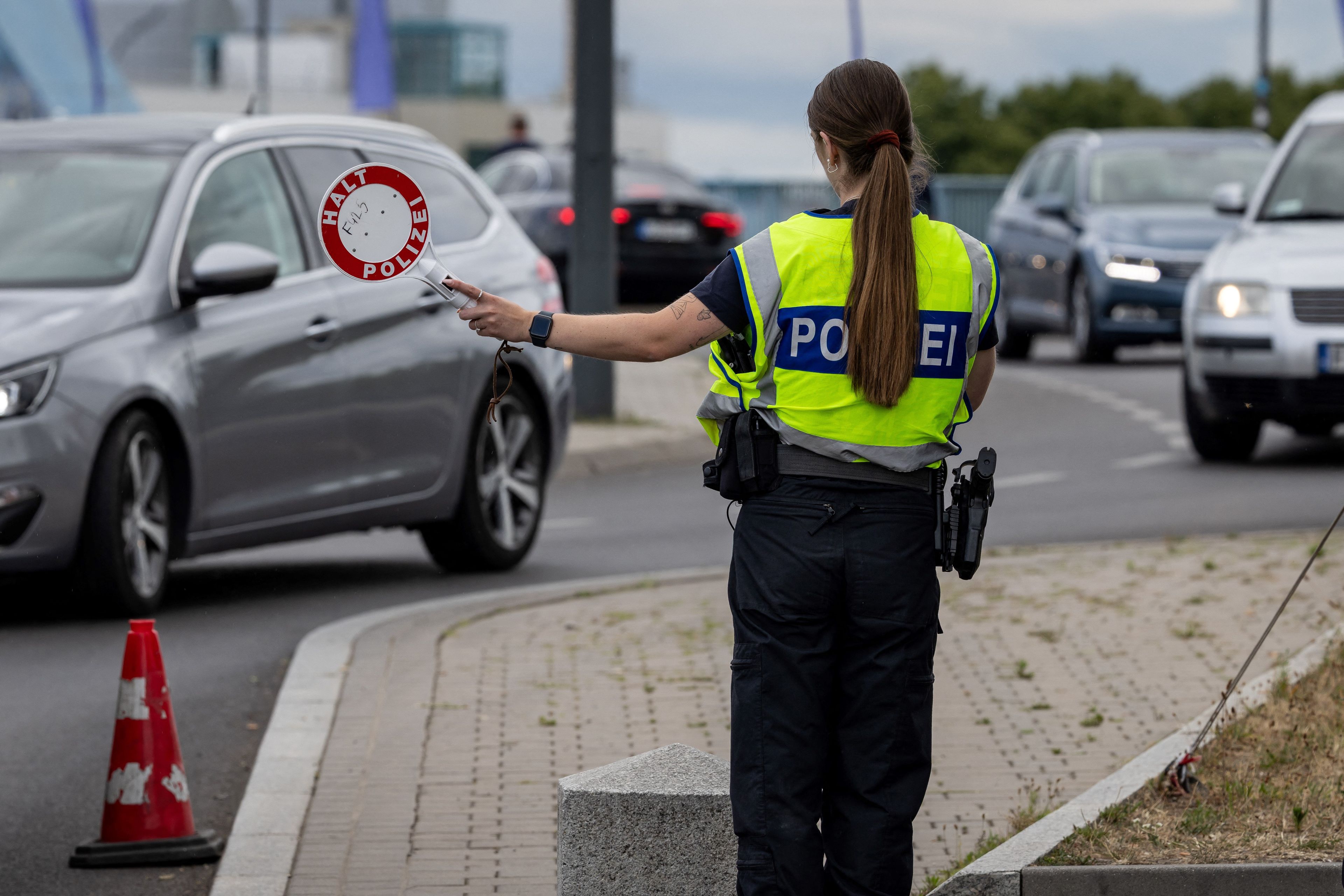 Kobieta w mundurze policyjnym z napisem Polizei na plecach zatrzymuje samochody czerwonym lizakiem z napisem Halt Polizei