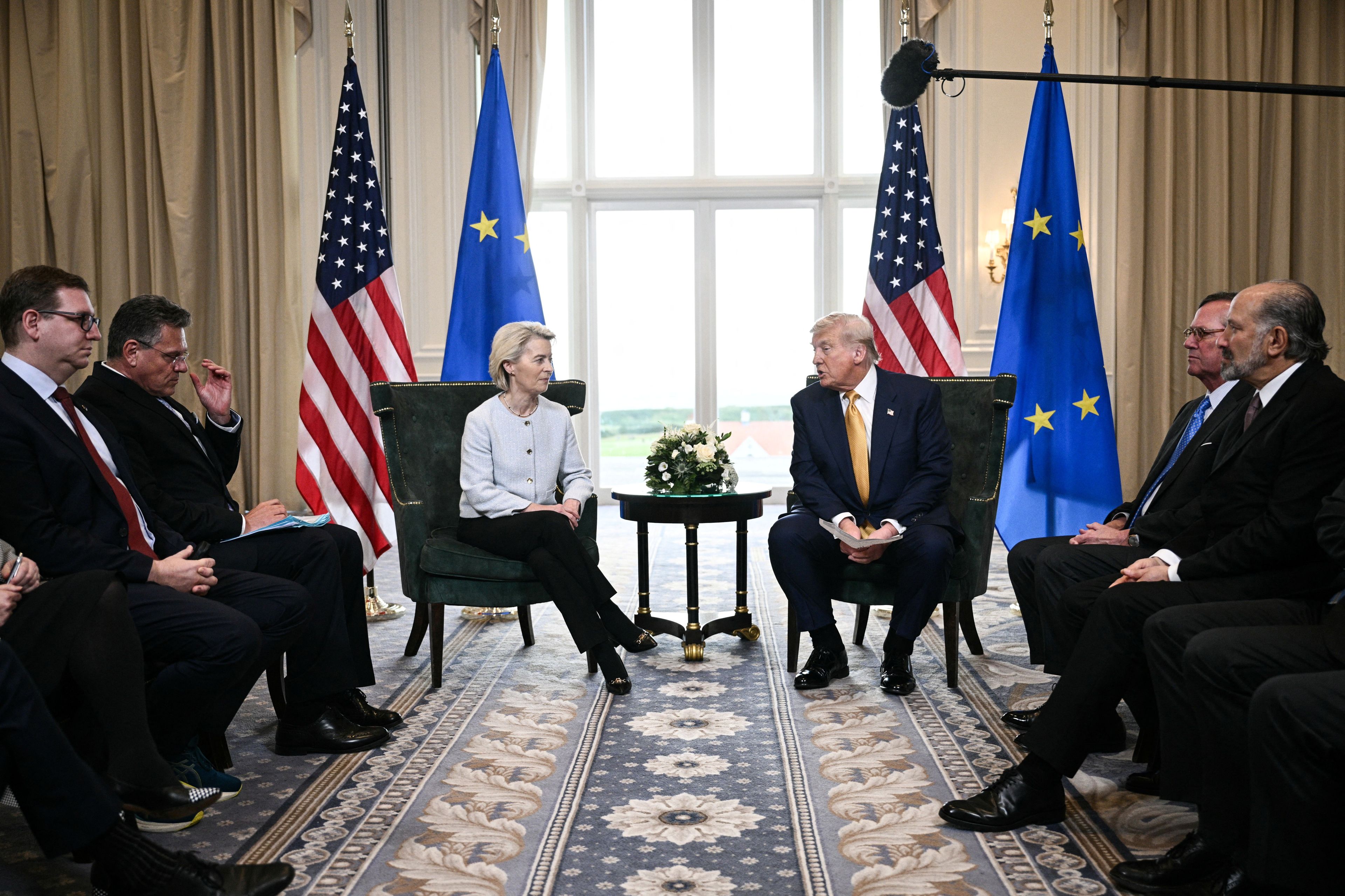 Donald Trump i Ursula von der Leyen przy stoliku na tle flag UE i USA