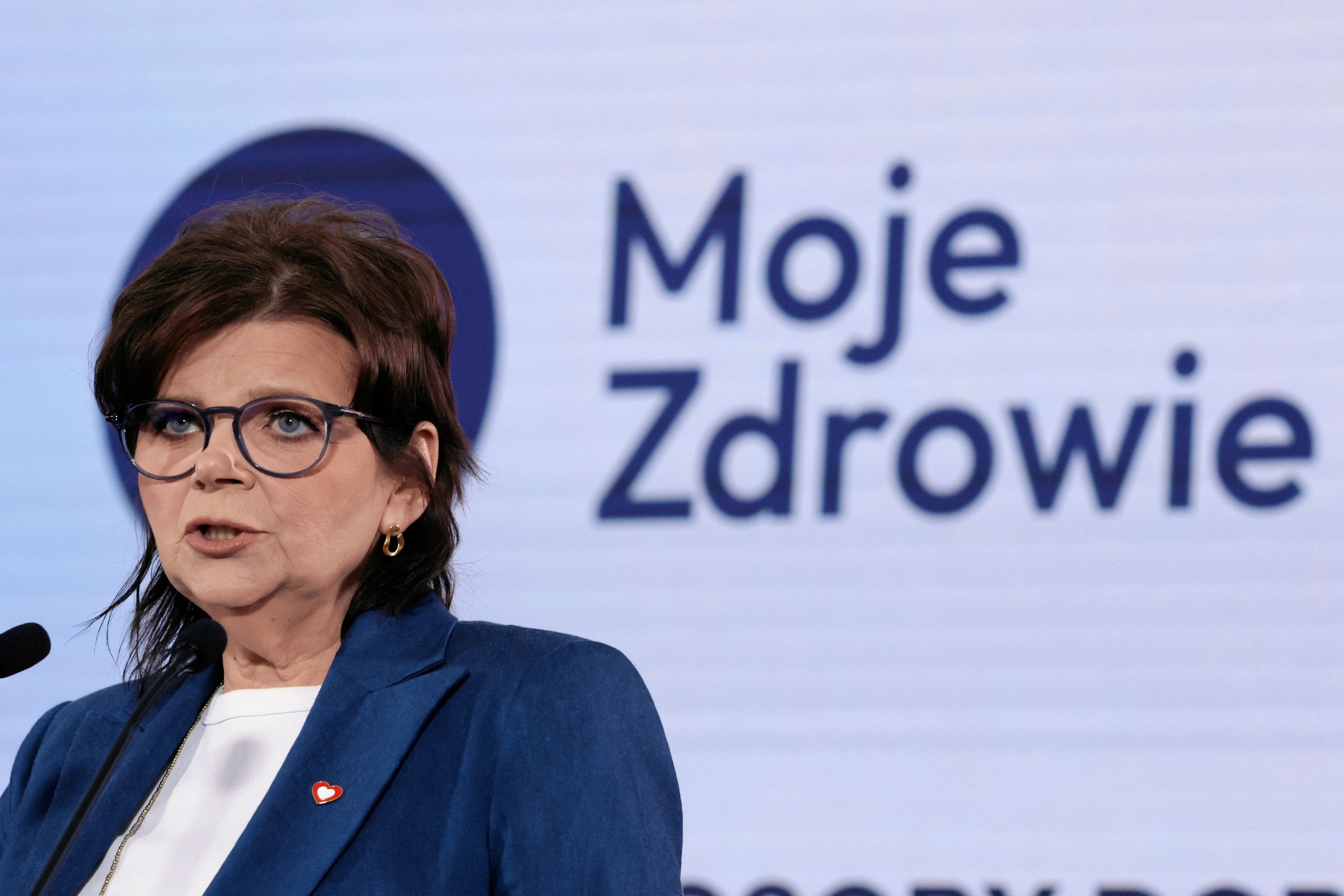 Kobieta w okulrach, w granatowej marynarce na tle planszy z napisem Moje Zdrowie