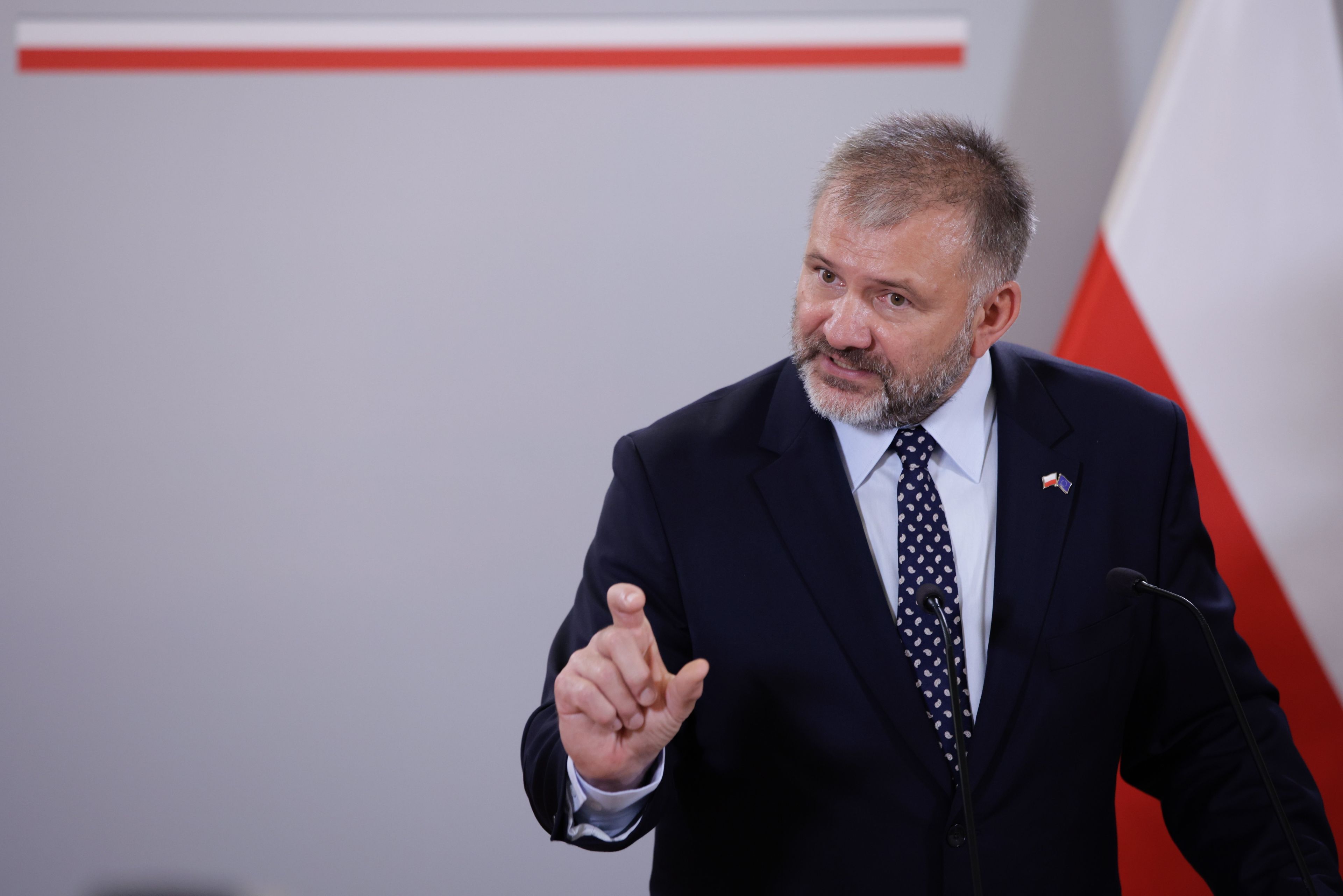 Krótko ostrzyżony siwawy mężczyzna mówi gestykulując