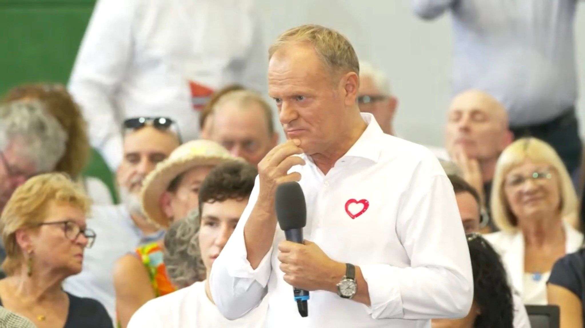 Zatroskany, otoczony ldxmi Donald Tusk w białej koszuli z czerwonym serduszkiem