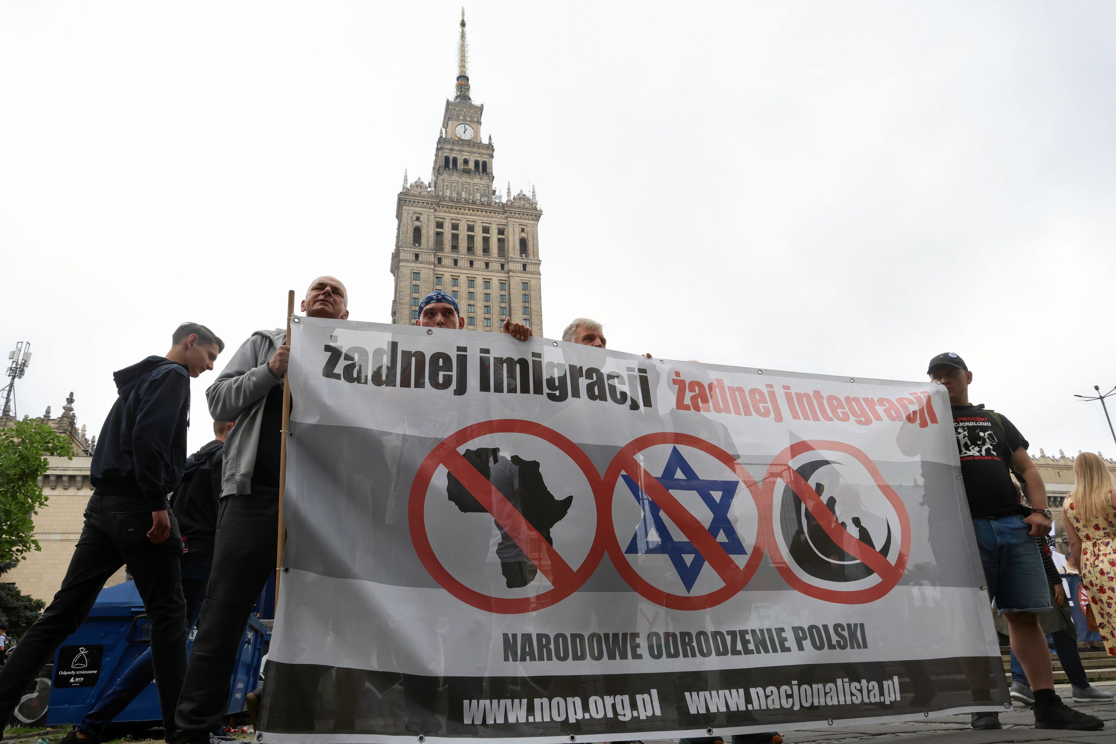 Plakat z napisem "żadnej imigracni z przekreśloną Afryką, Gwiazdą Dawida i Półksieżycen. Za nim Pałac Kultury w Warszawie