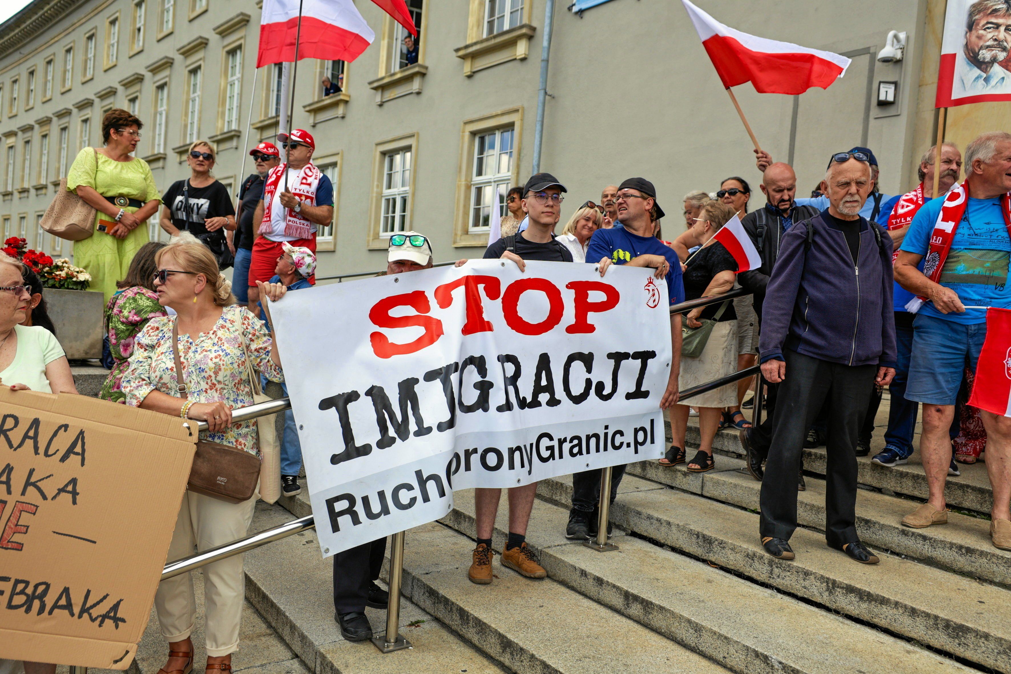 Kilkanaście osób stoi na schodach budynku z transparentem STOP IMIGRACJI