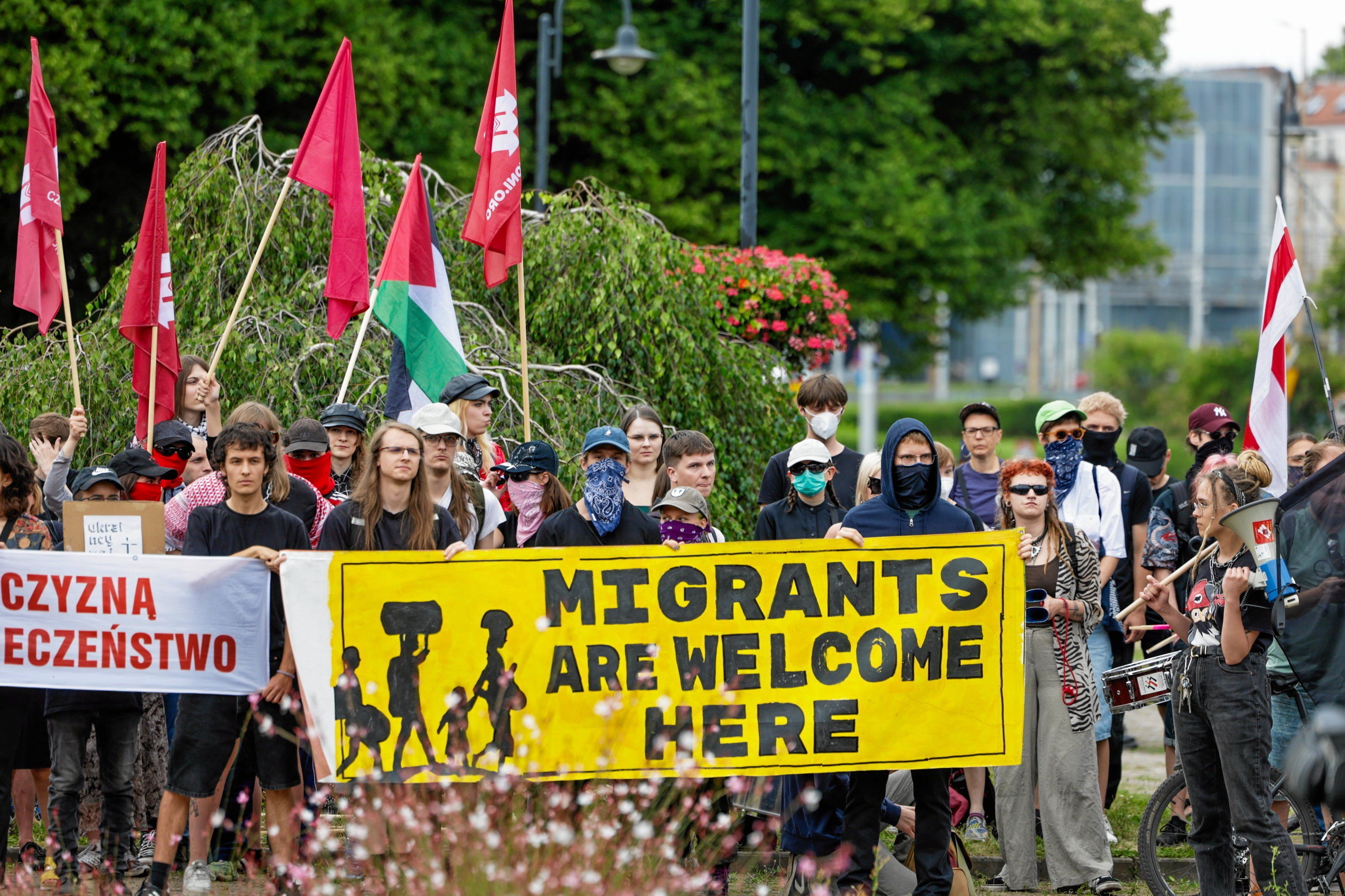 Na zdjęciu jest gropa ludzi, trzymają żółty plakat z napisem: "Migrants are welcome here"