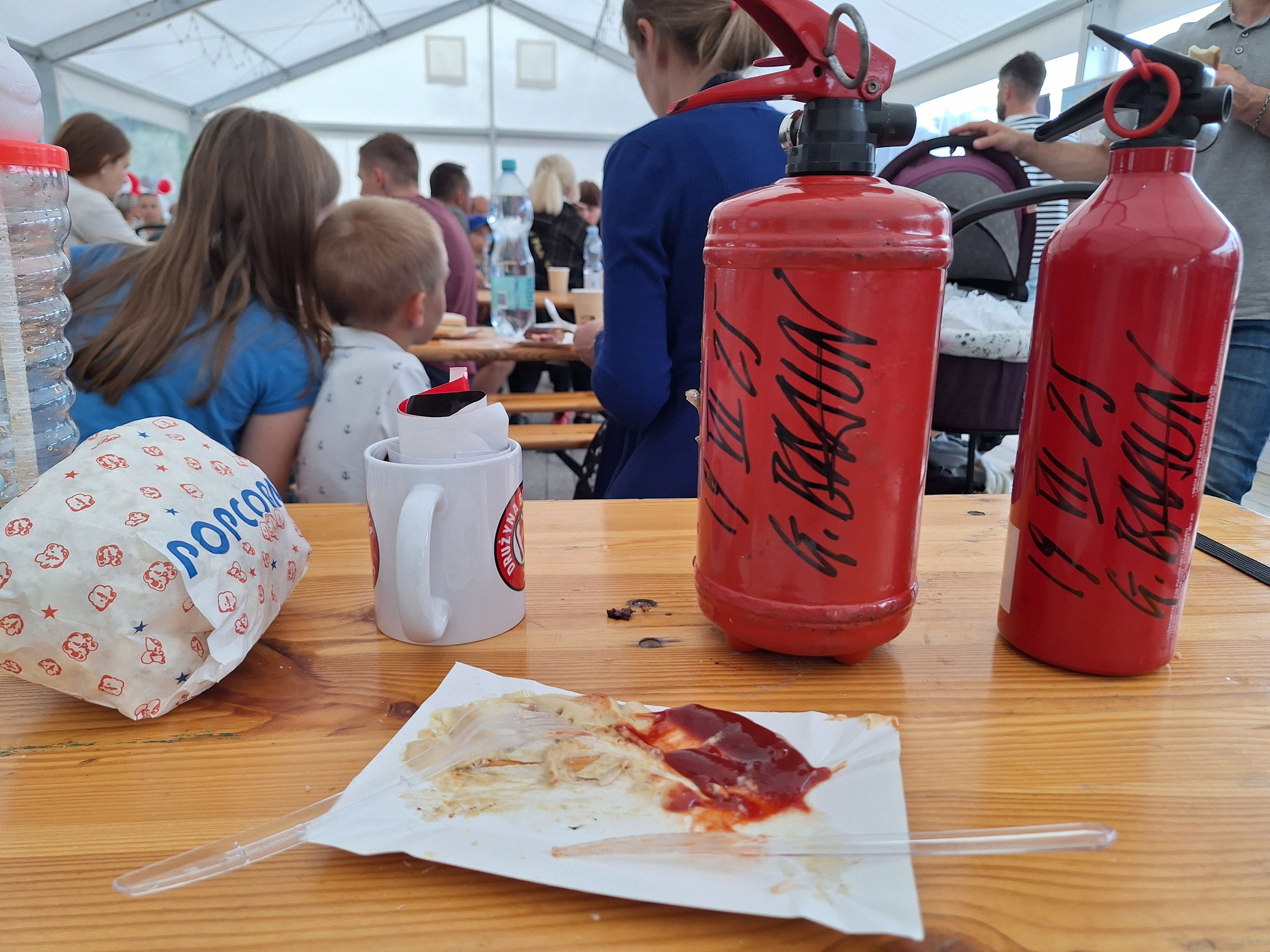 Na stole leży plastikowy talerzyk z resztkami po ketchupie, obok dwie gaśnice z autografem Grzegorza Brauna.