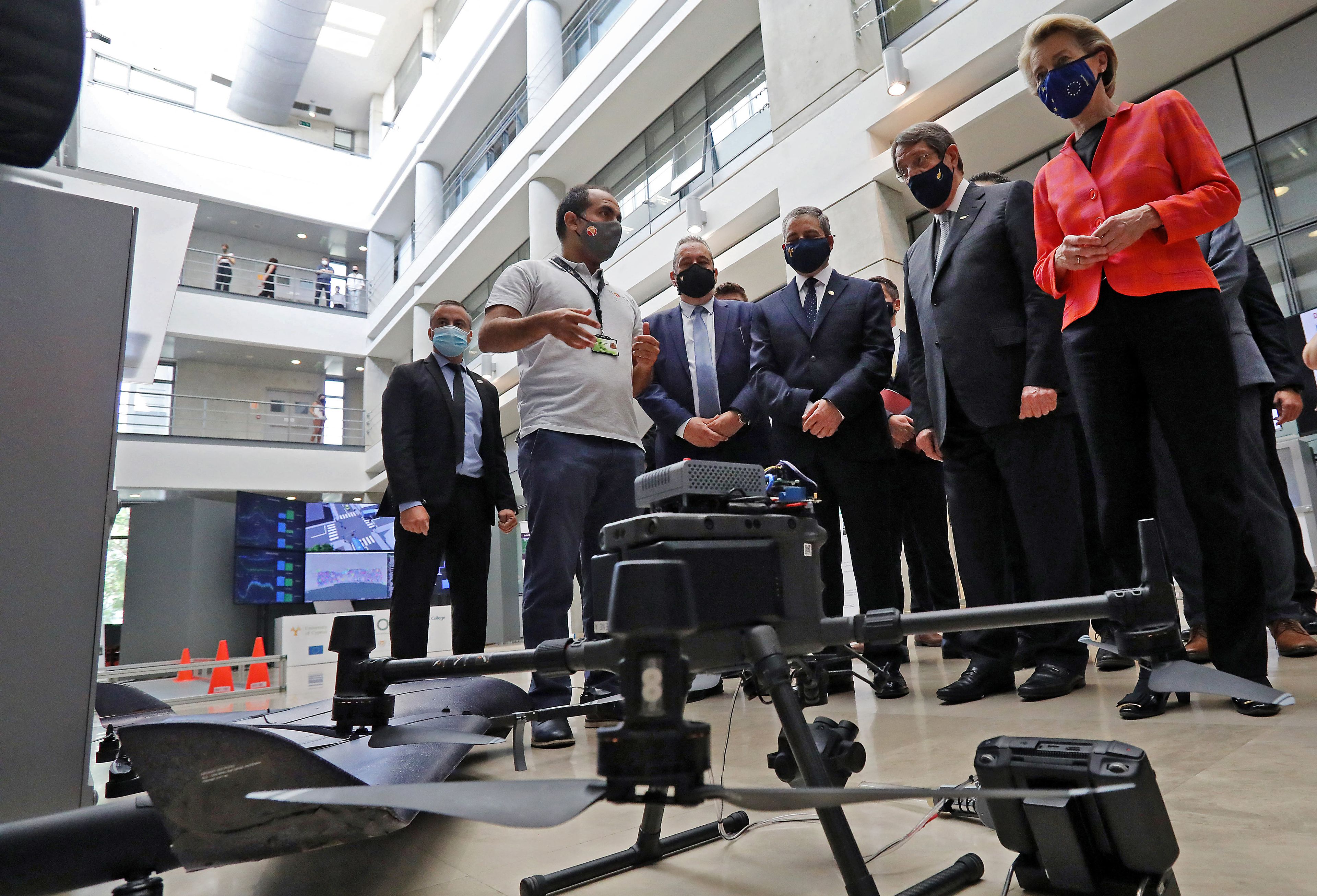 Grupa ludzi w covidowych maseczkach stoi wokół drona