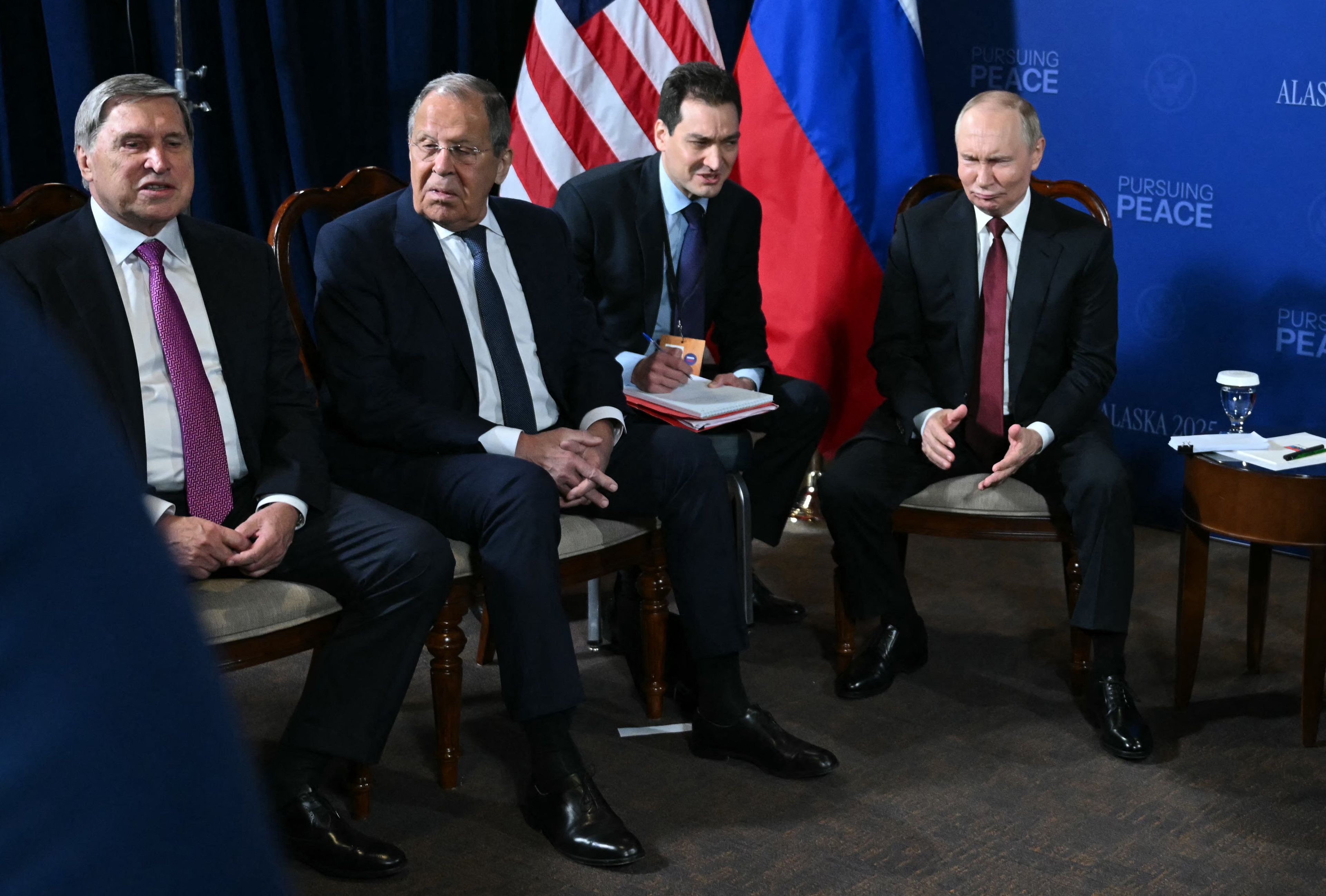 czterech męzczyzn w garniturach siedzi na krzesłach: Uszakow, Ławrow, tłumacz i Putin