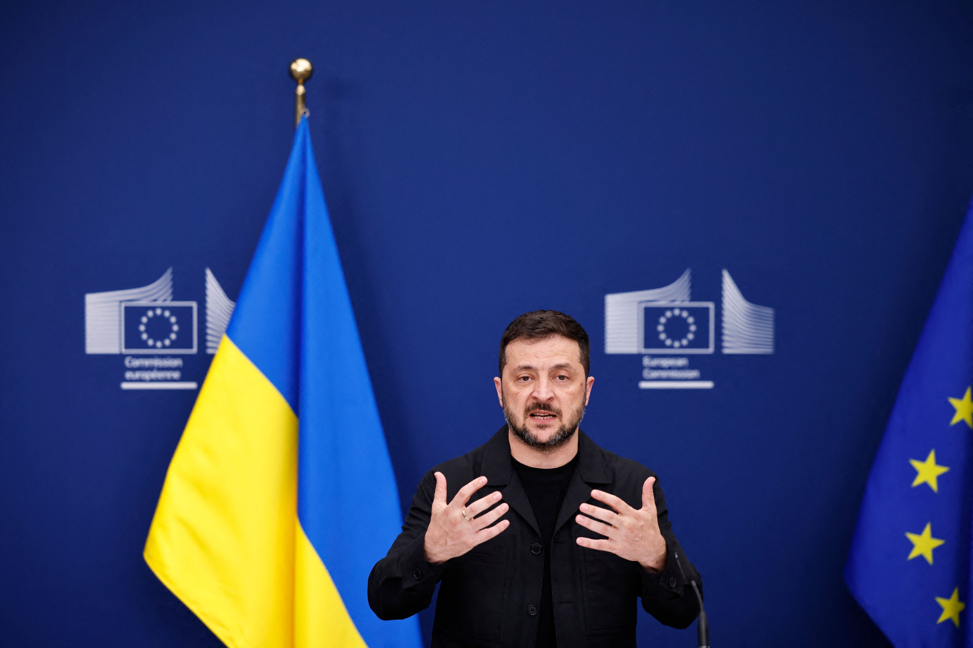 Na zdjęciu jest mężczyzna ok. 45 lat. Ma czarne włosy i brodę, ubrany w czarną bluzę. Po lewej stoi flaga niebiesko-żółta