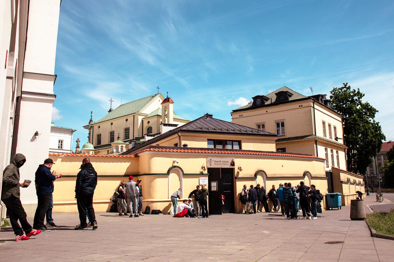 Zdjęcie. Grupa ludzi przed zabudowaniami klasztornymi.