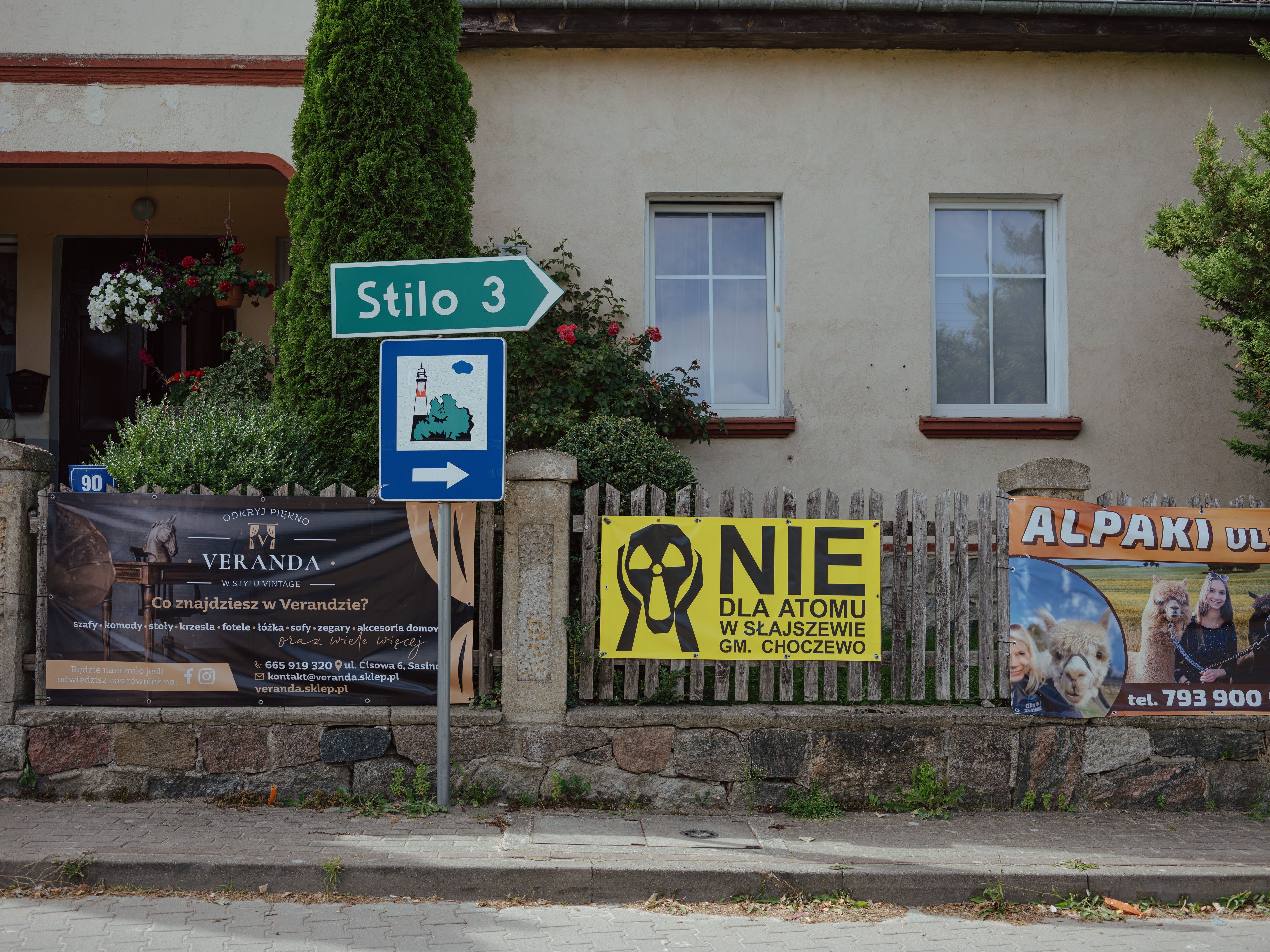płot przy domu w gminie Choczewo z dwoma banerami reklamującymi turystykę i jednym antyatomowym