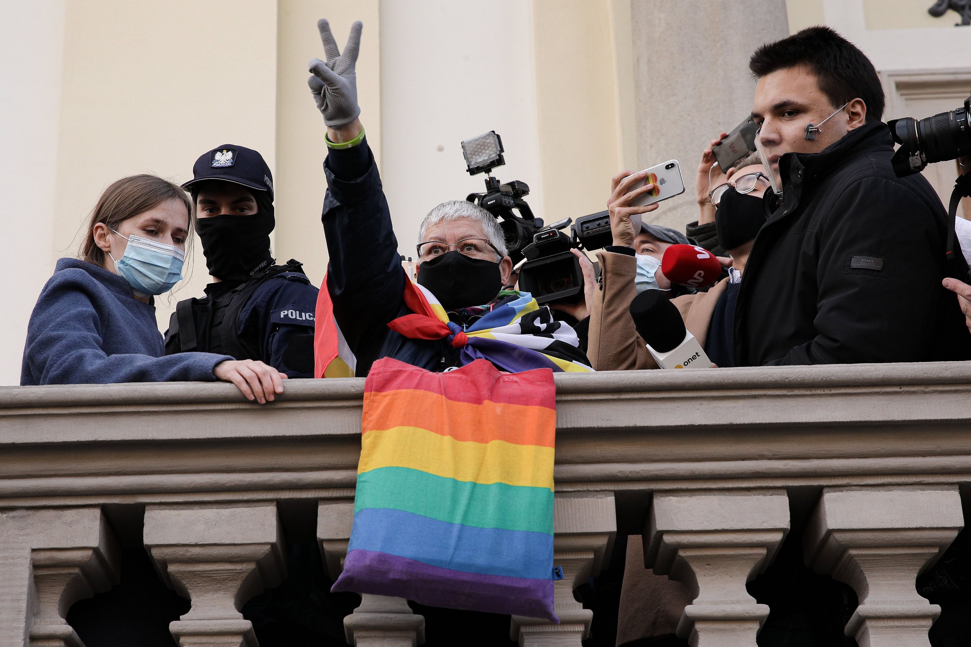 Kobieta z poniesioną ręką pokazuje symbol zwycięstwa, obok niej tłum i policja