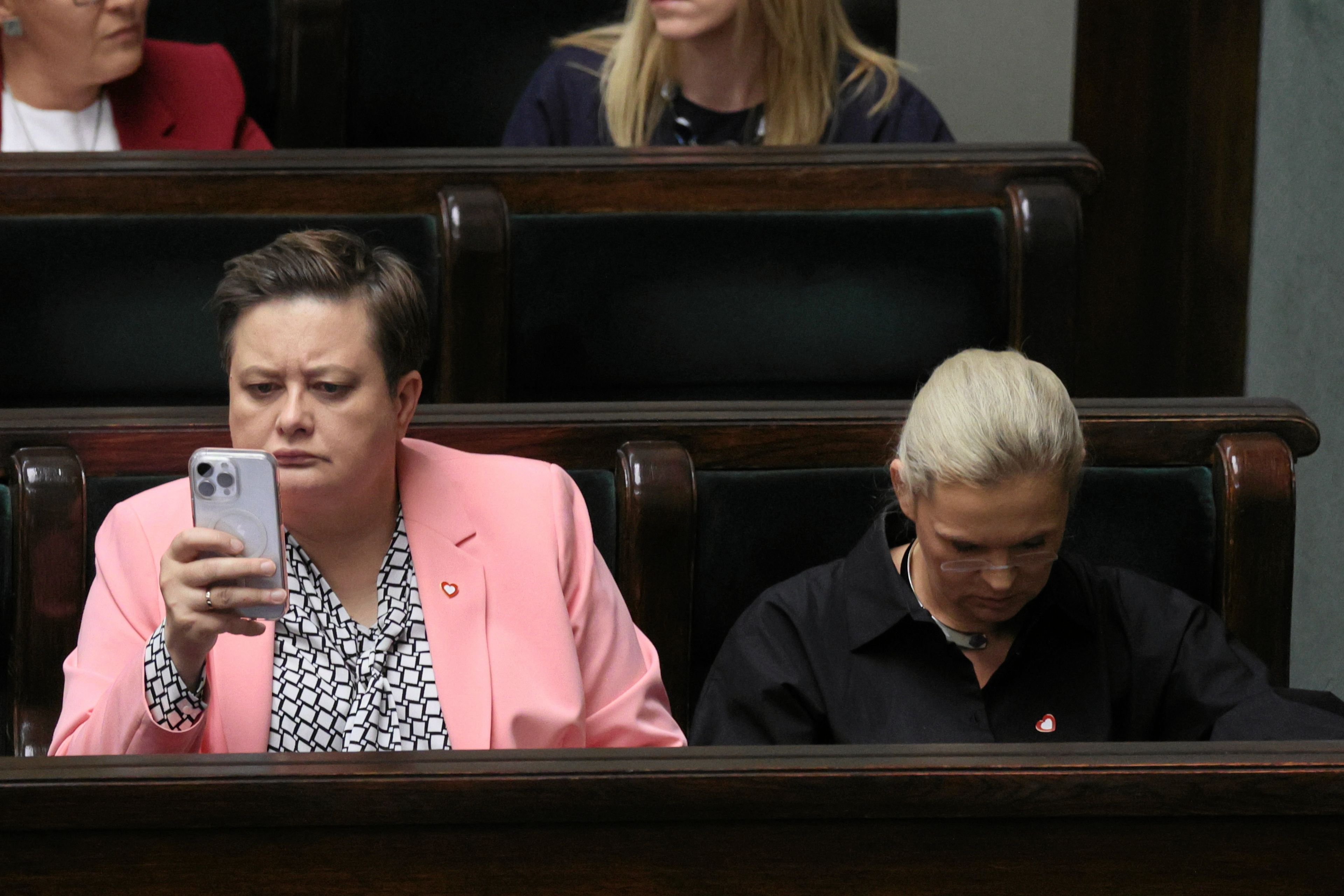 Katarzyna Lubnauer i Barbara Nowacka siedzą w ławie sejmowej. Lubnauer patrzy w telefon, Nowacka spuszcza głowę
