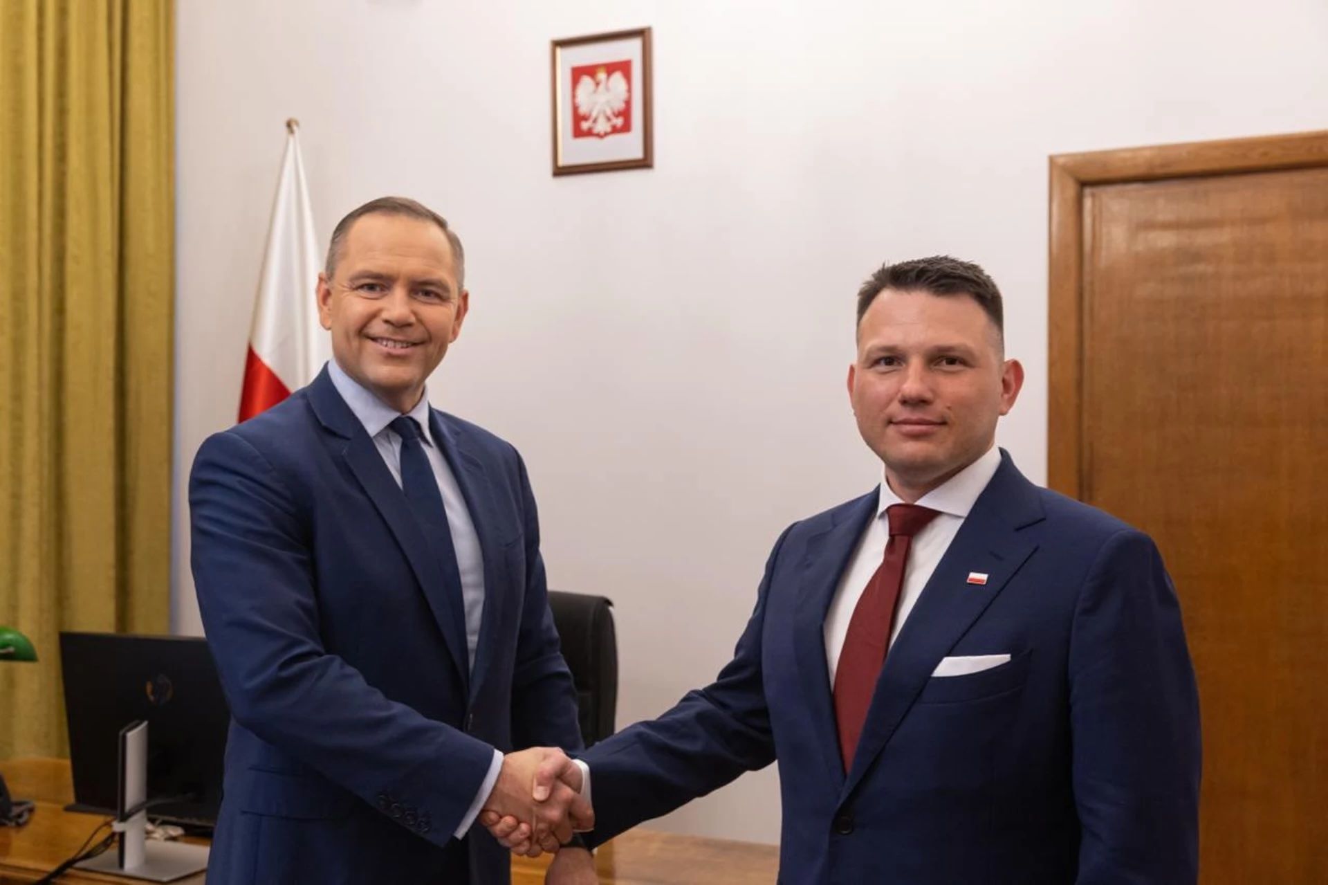Karol Nawrocki i Sławomir Mentzen ściskają dłonie. W tle godło Polski