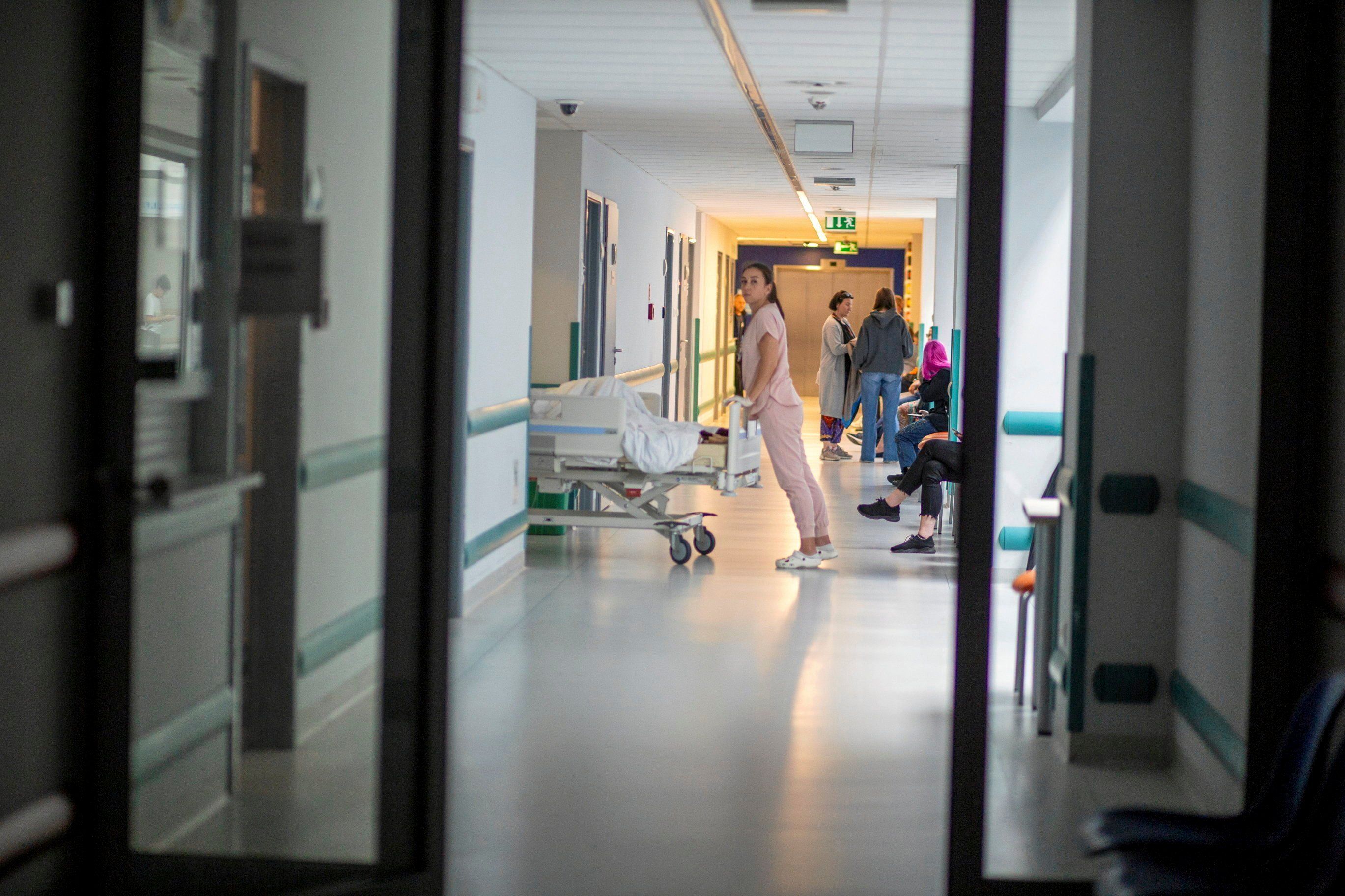 Korytarz szpitalny, pielęgniarka pcha łóżko z pacjentem.
