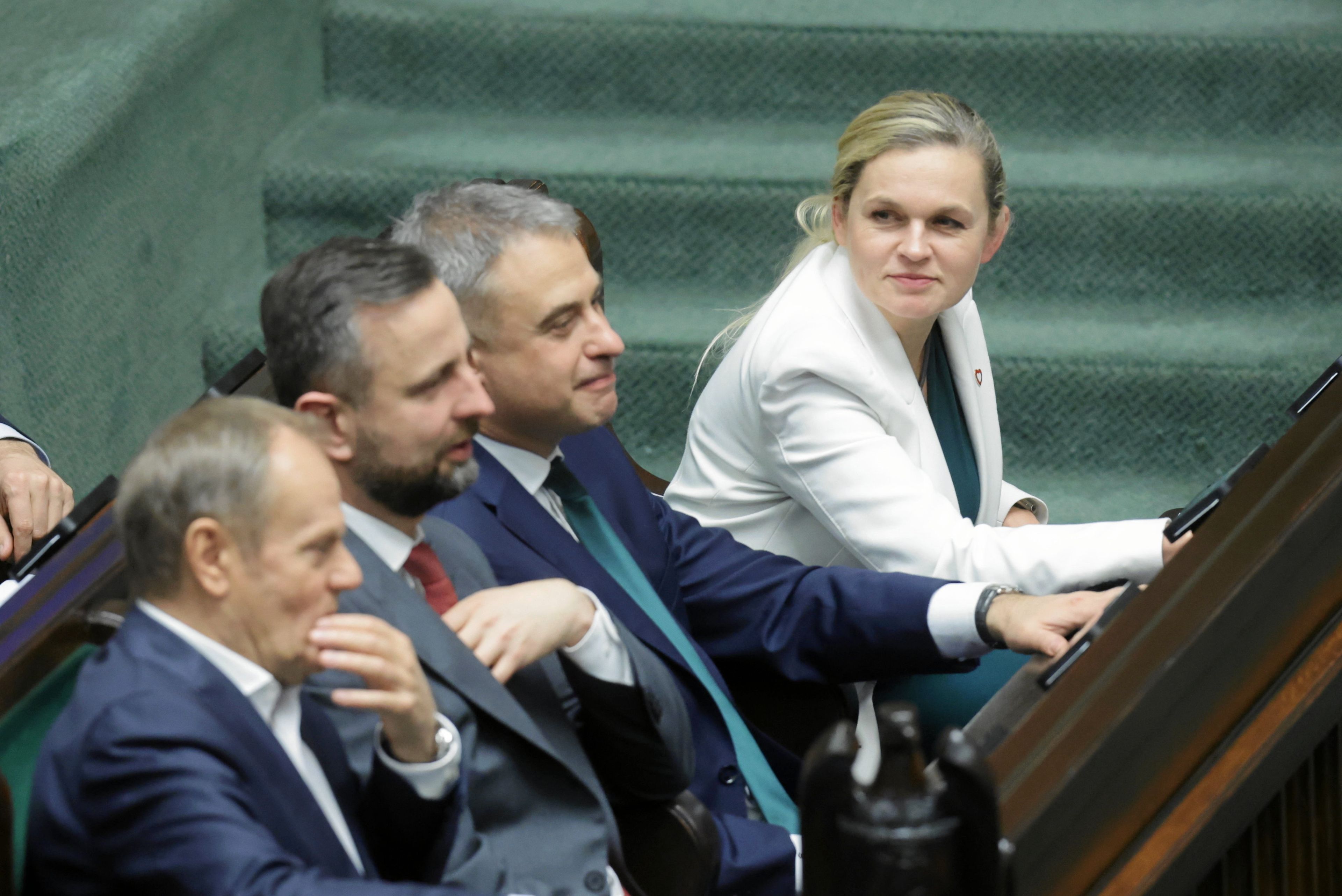 Kobieta w białym kostiumie obok trzech mężczyzna w garniturach i krawatach