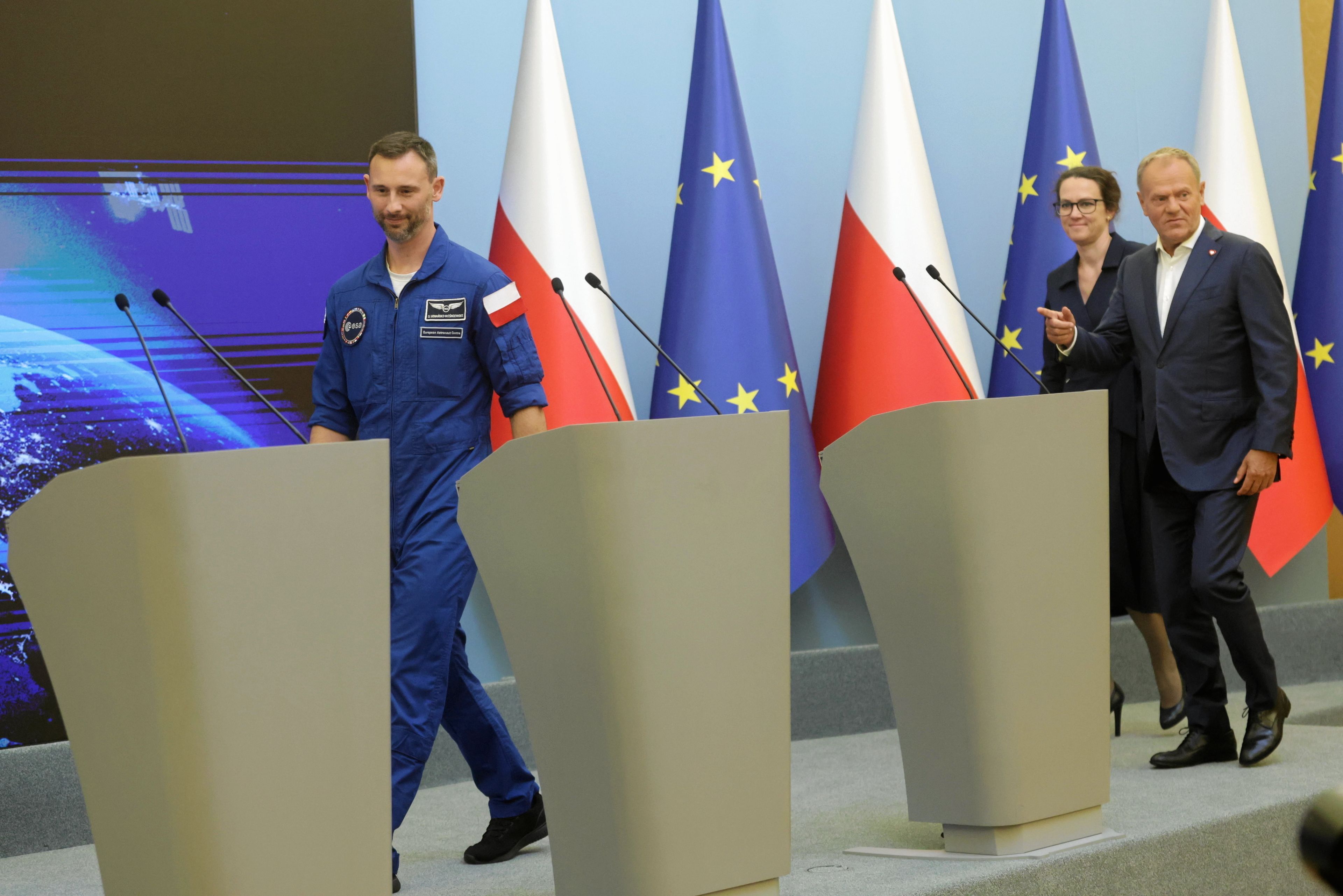 Sławosz Uznański Wiśniewski, Donald Tusk i Marta Wachowicz (szefowa POLSA) wchodzą do sali, gdzie odbywała się konferencja prasowa po lądowaniu misji Ignis