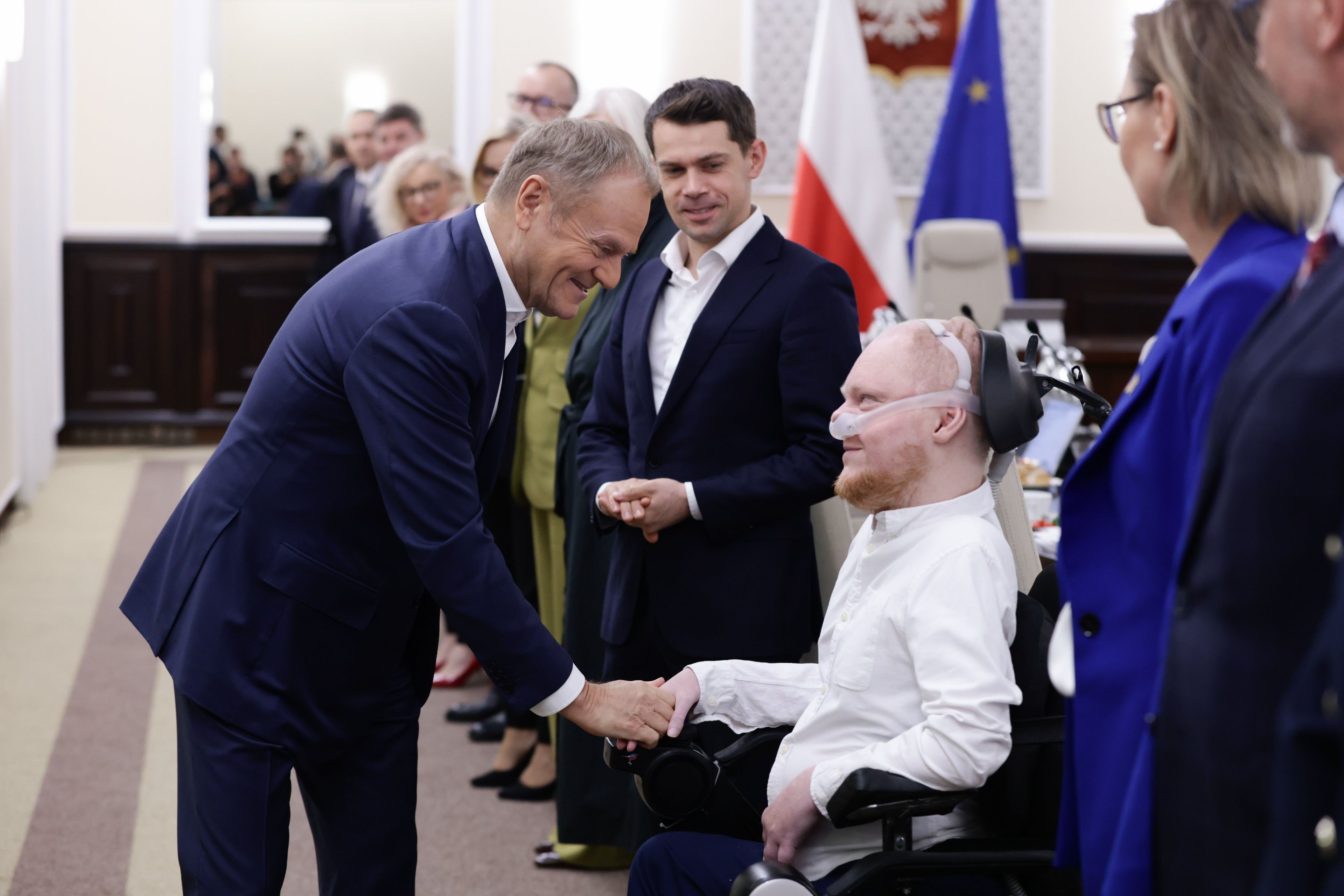 Mężczyzna w garniturze ściska dłoń mężczyzny na wózku inwalidzkim