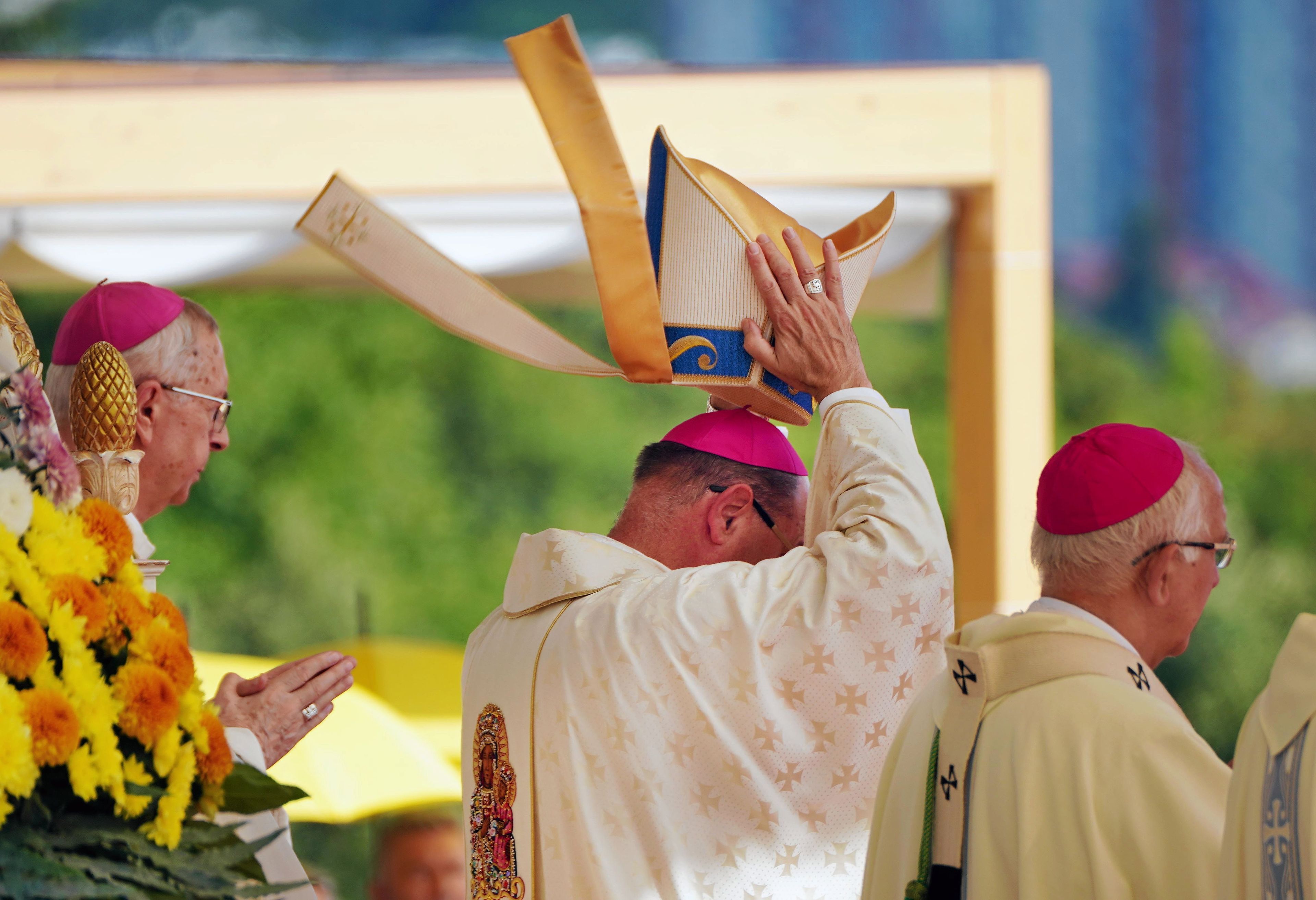 Biskup w szacie liturgicznej nakładający sobie na głowę infułę.