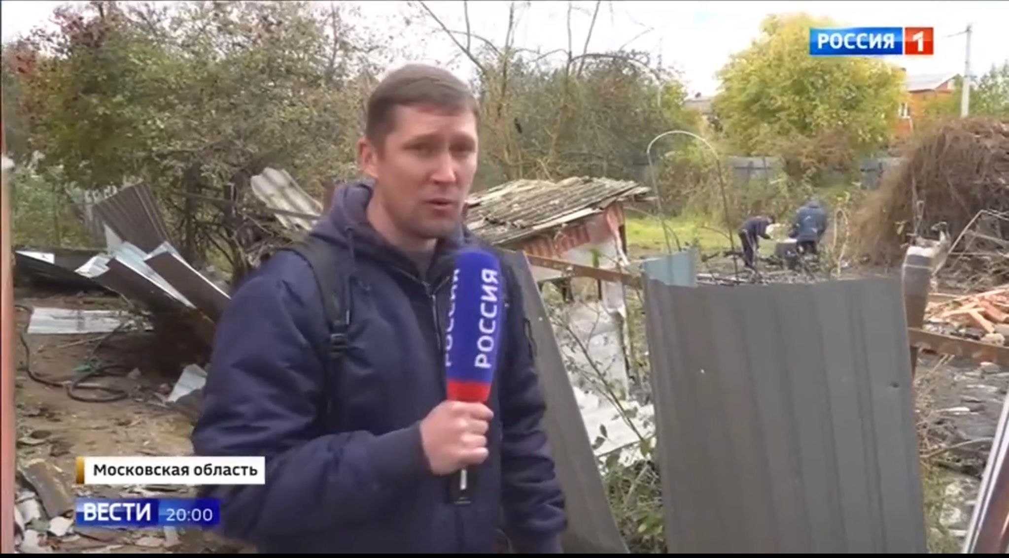 Mężczyznma z mikrofonem Rossija 1 na tle zniszczonefo domu