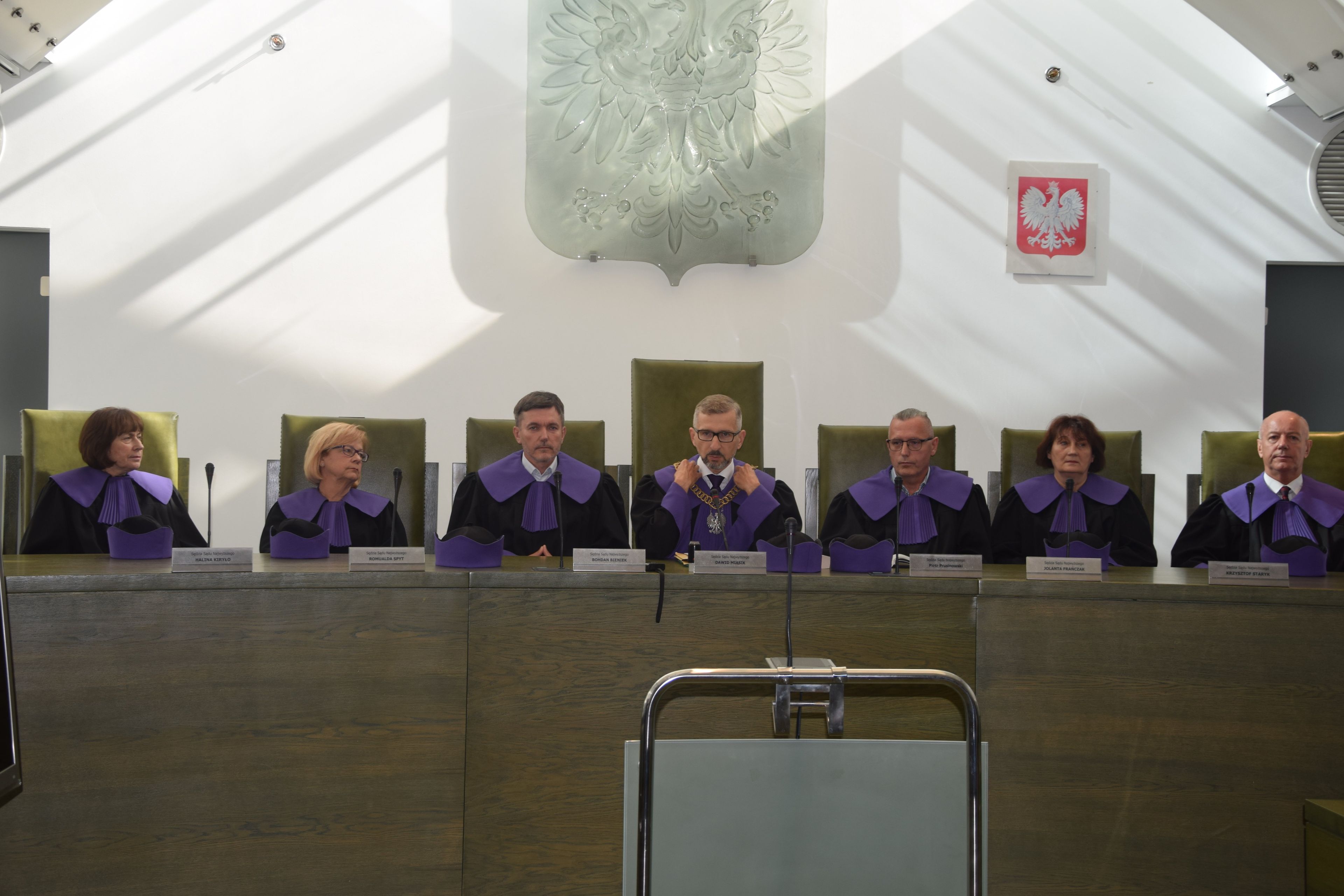 Kilka osób zasiada za długim stołem w fioletowych strojach sędziowskich