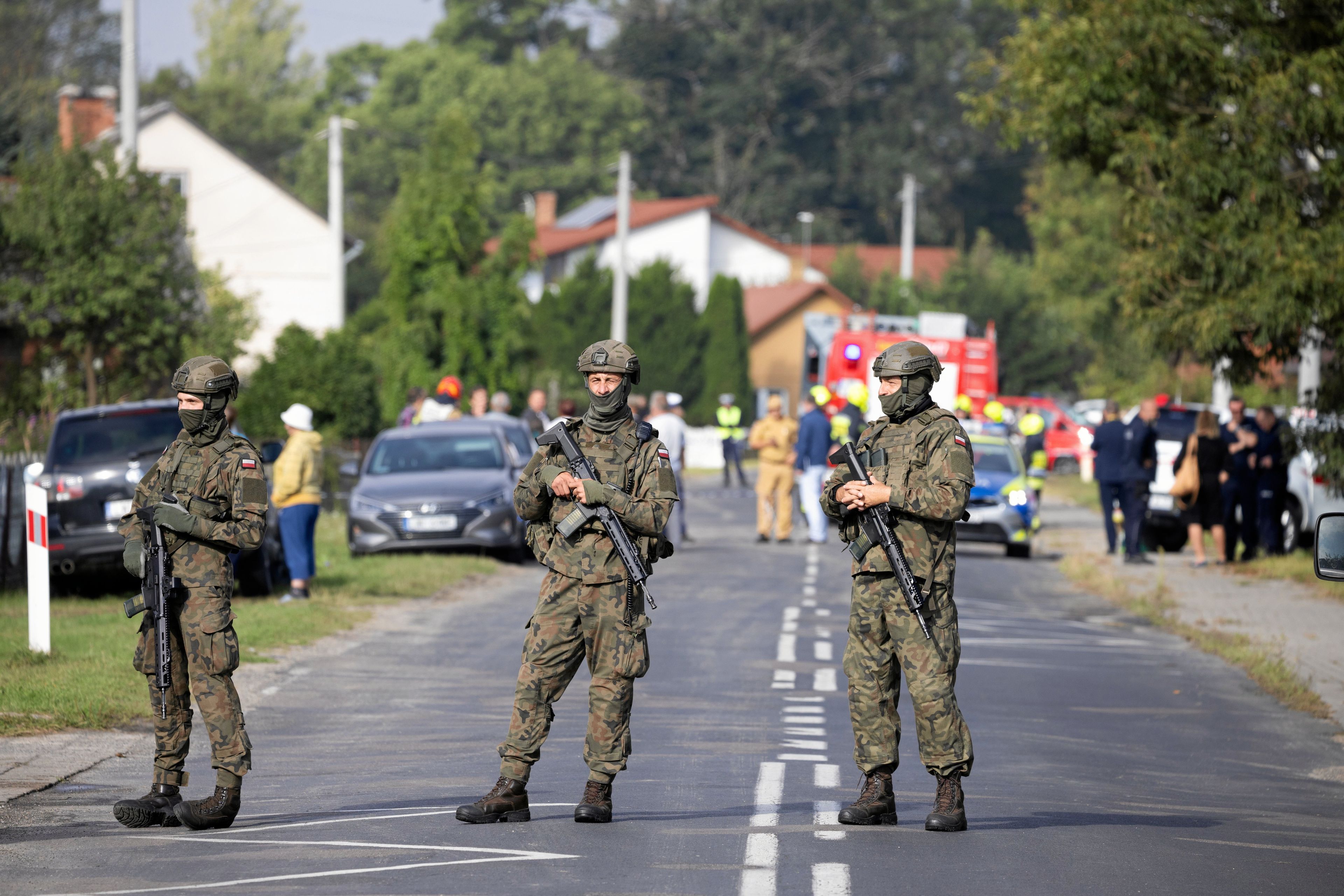 Trzech żołnierzy w pełnym bojowym rynsztunku z bronią długą stoją na środku drogi w miasteczku Wyryki
