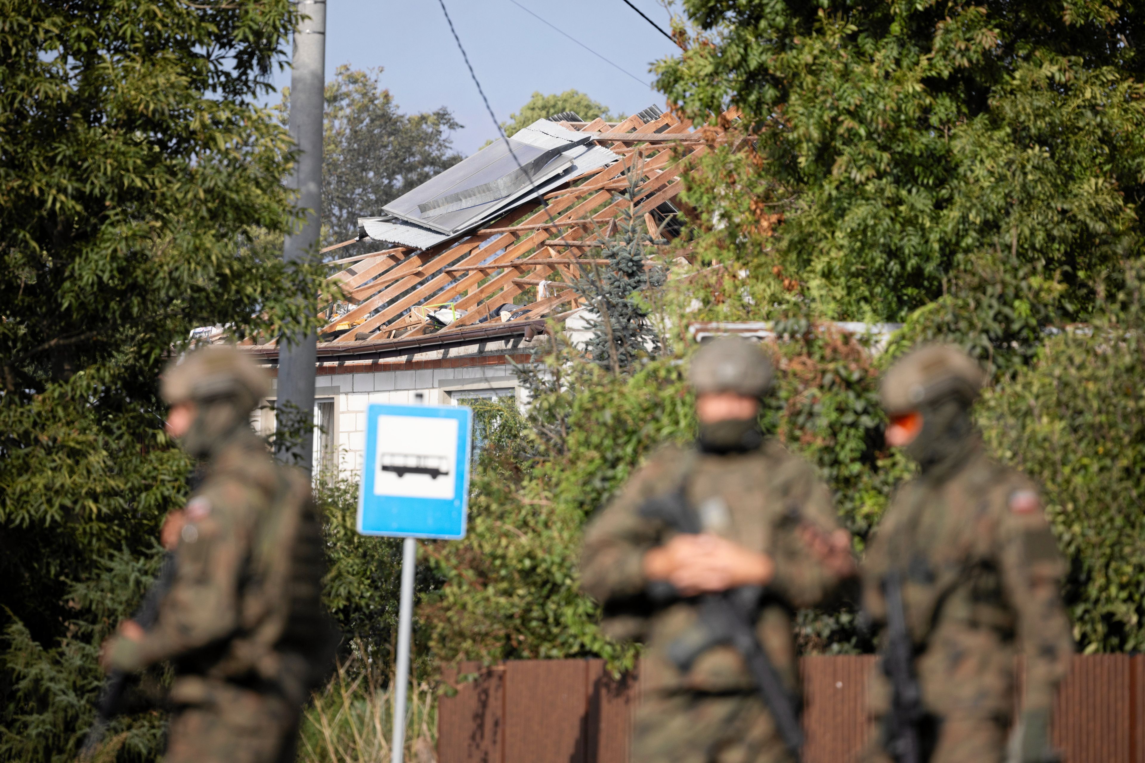 Na zdjeciu jest dwóch meżczyzn w kamuflażu, w tle widać uszkodzony dach domu