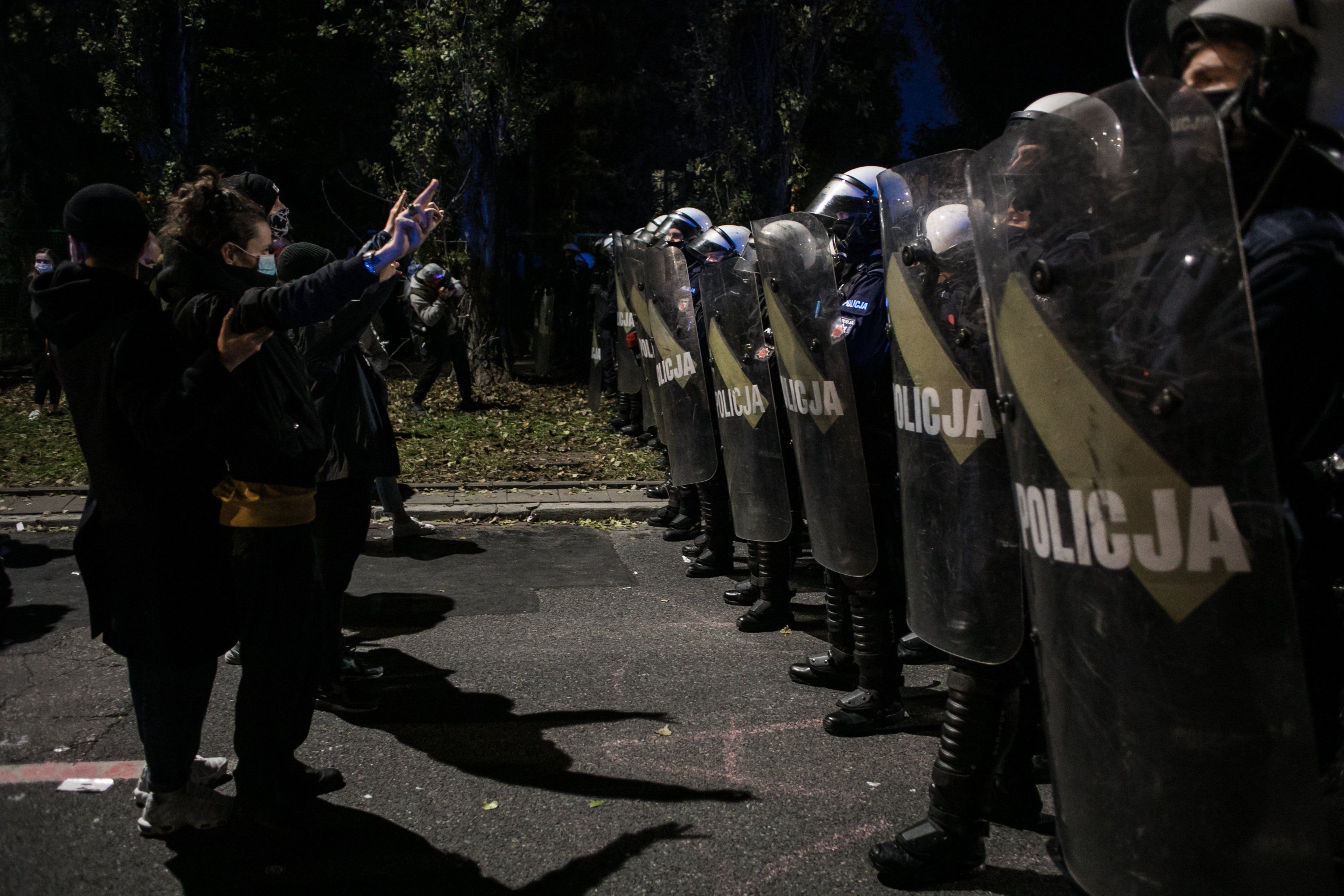 Młode kobiety stoja naprzeciwko szpaleru policjantów w kaskach i z tarczami