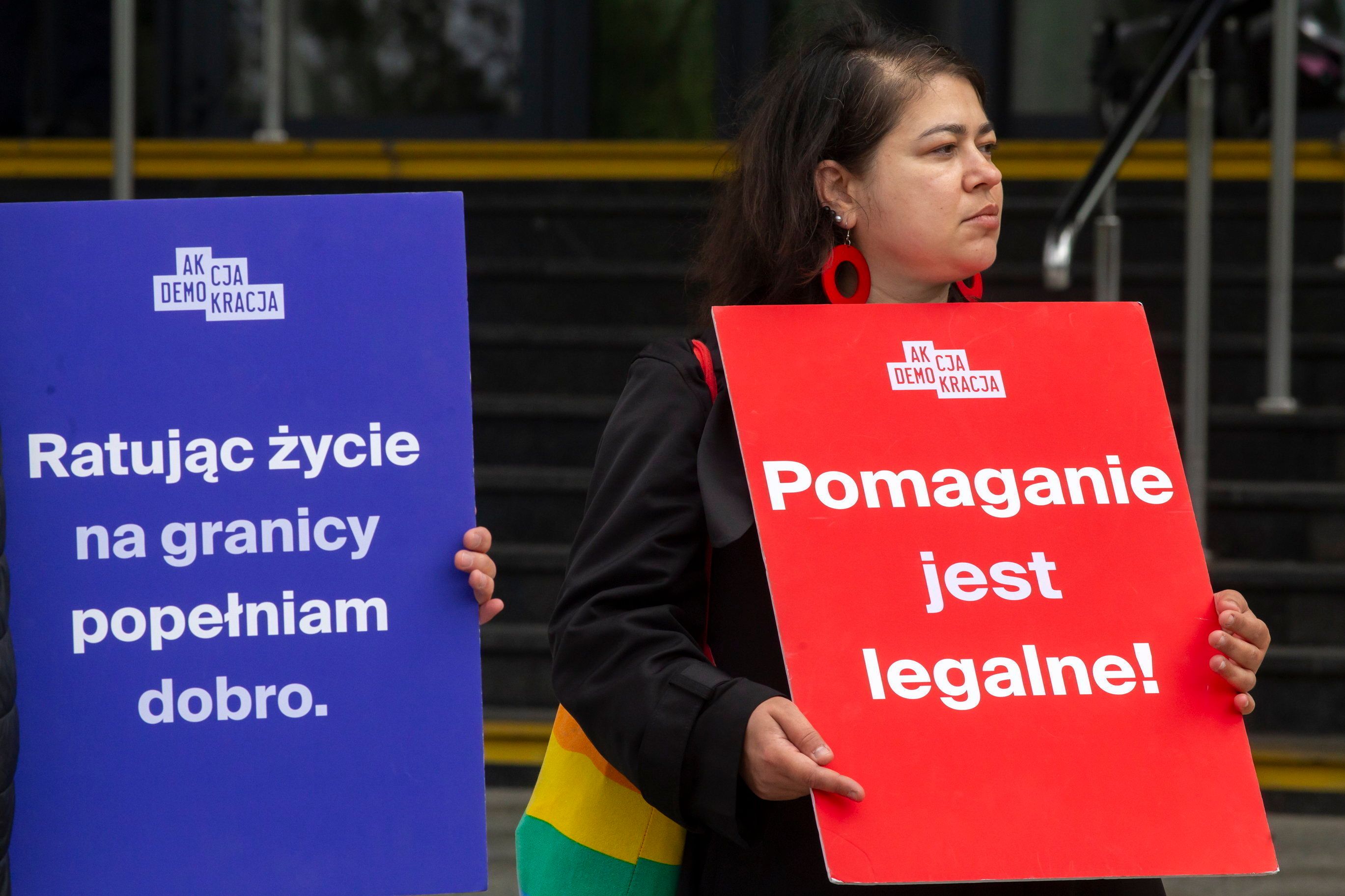 Luzie trzymają dwa transparenty. Niebieski "Ratując życie na granicy popełniam dobro" 0 czerwony "Pomaganie jest legalne")