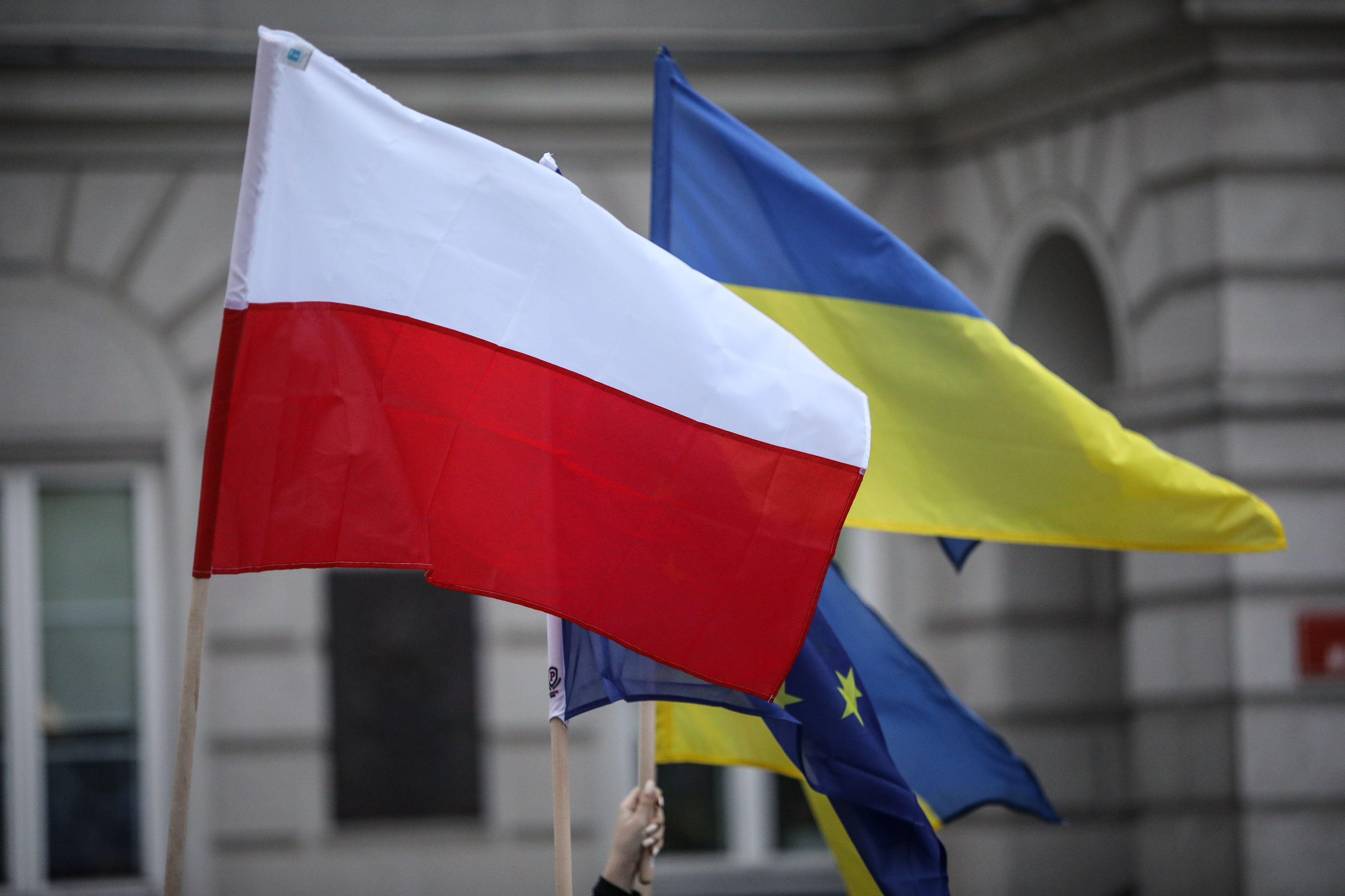 Flaga Polski, flaga Ukrainy i flaga Unii Europejskiej. W tle mury budynku w stylu neoklasycznym