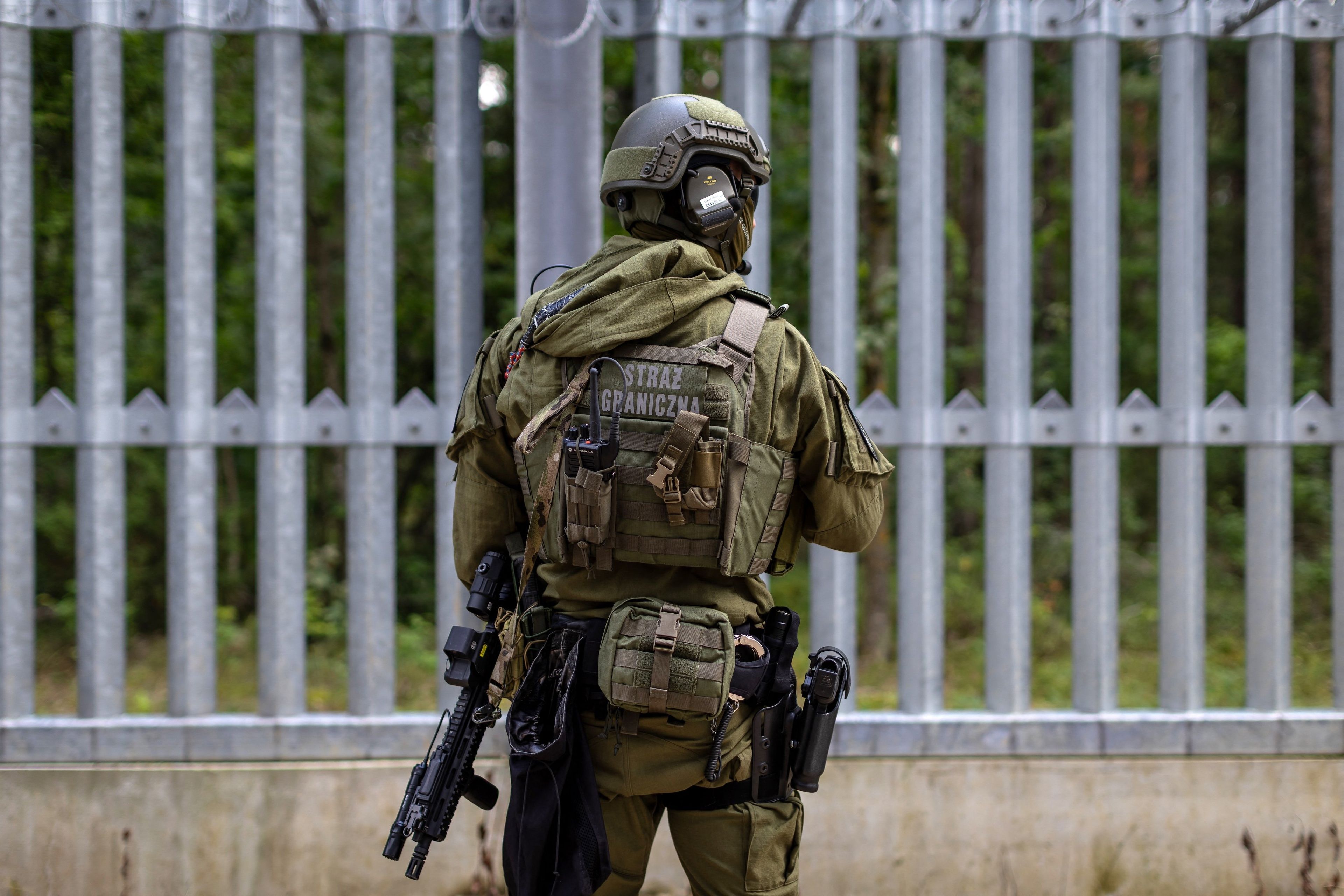 Polski funkcjonariusz Straży Granicznej stoi na granicy polsko-białoruskiej przed ogrodzeniem granicznym