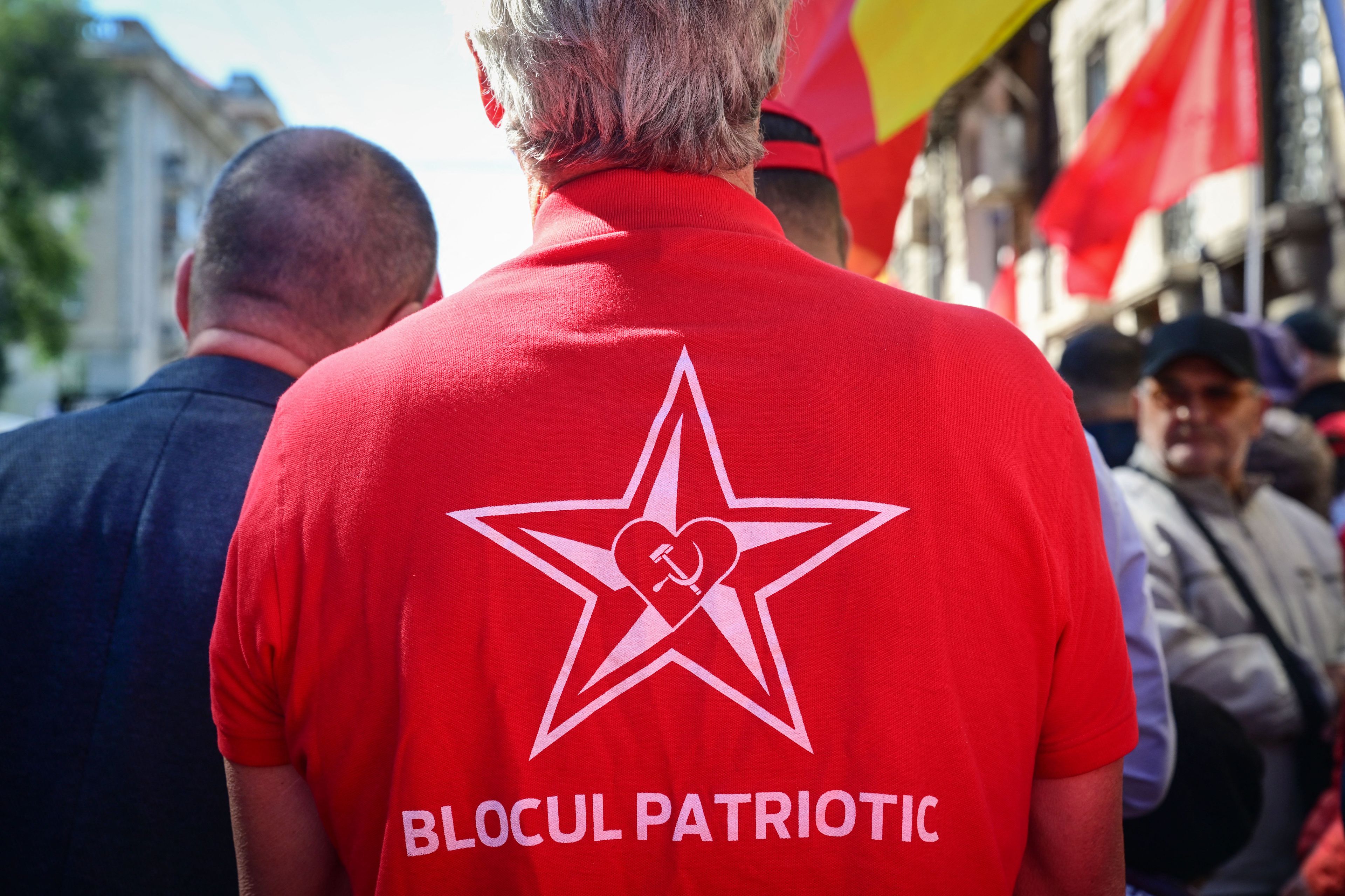 Sfotografowany od tyłu męzczyzna w czerwonej bluzie z gwiazdą, sierpem i młotem i napisem "Blocul patriotic"