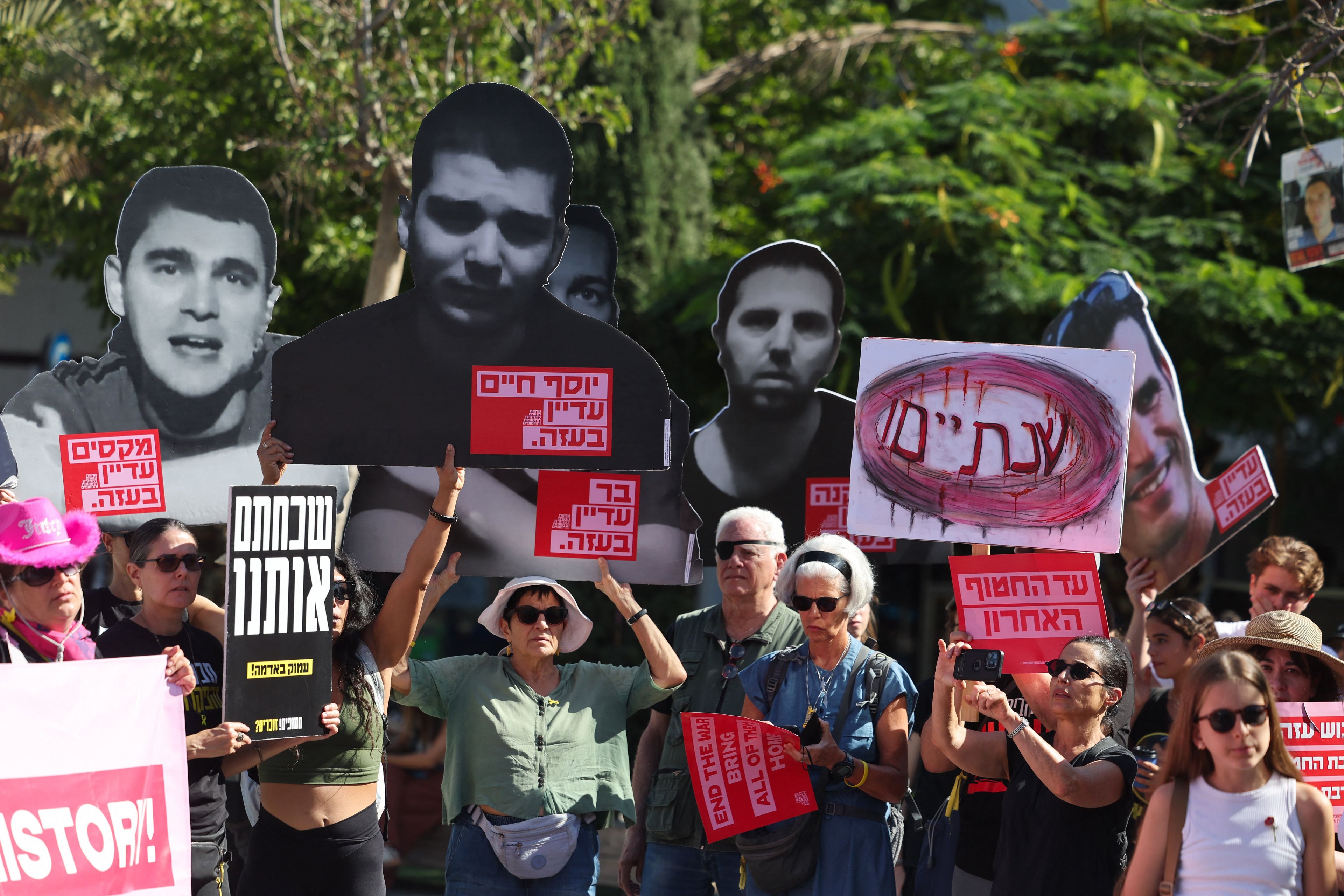 Tłum protestujący z plakatami po hebrajsku i tekturowymi postaciami na zdjęciach.
