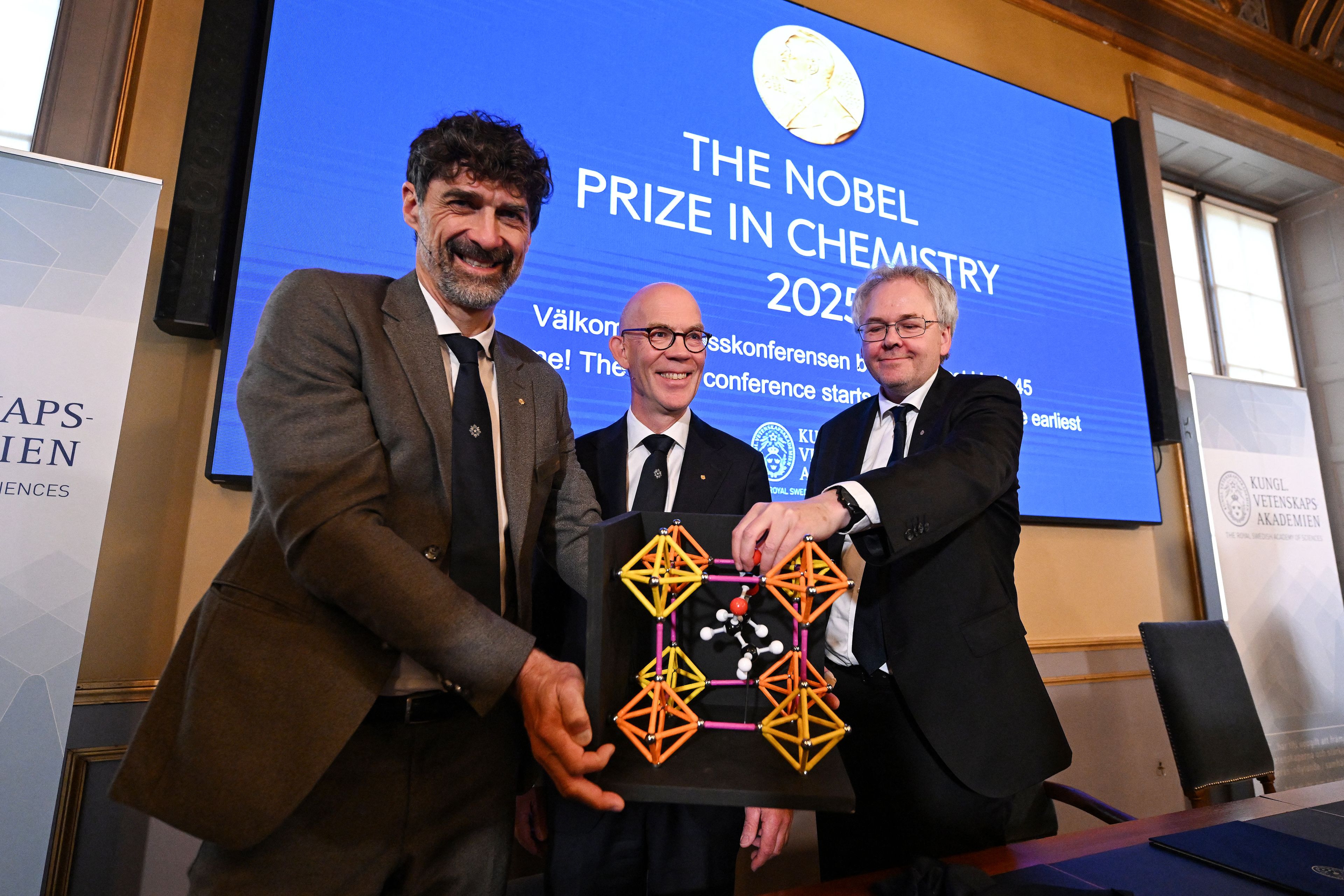 (LtoR) Heiner Linke, Chair of the Nobel Committee for Chemistry, Hans Ellegren, Secretary General of The Royal Swedish Academy of Sciences, and Olof Ramstroem, Member of the Nobel Committe for Chemistry, pose with a model during a press conference to announce Japan's Susumu Kitagawa, UK-born Richard Robson and American-Jordanian Omar M Yaghi as the winners of the 2025 Nobel Prize in Chemistry at the Royal Swedish Academy of Sciences in Stockholm, Sweden, on October 8, 2025. Japan's Susumu Kitagawa, UK-born Richard Robson and American-Jordanian Omar M. Yaghi won the Nobel Prize in Chemistry for developing so-called metalorganic frameworks, the Nobel jury said on October 8, 2025. (Photo by Jonathan Nackstrand / AFP)