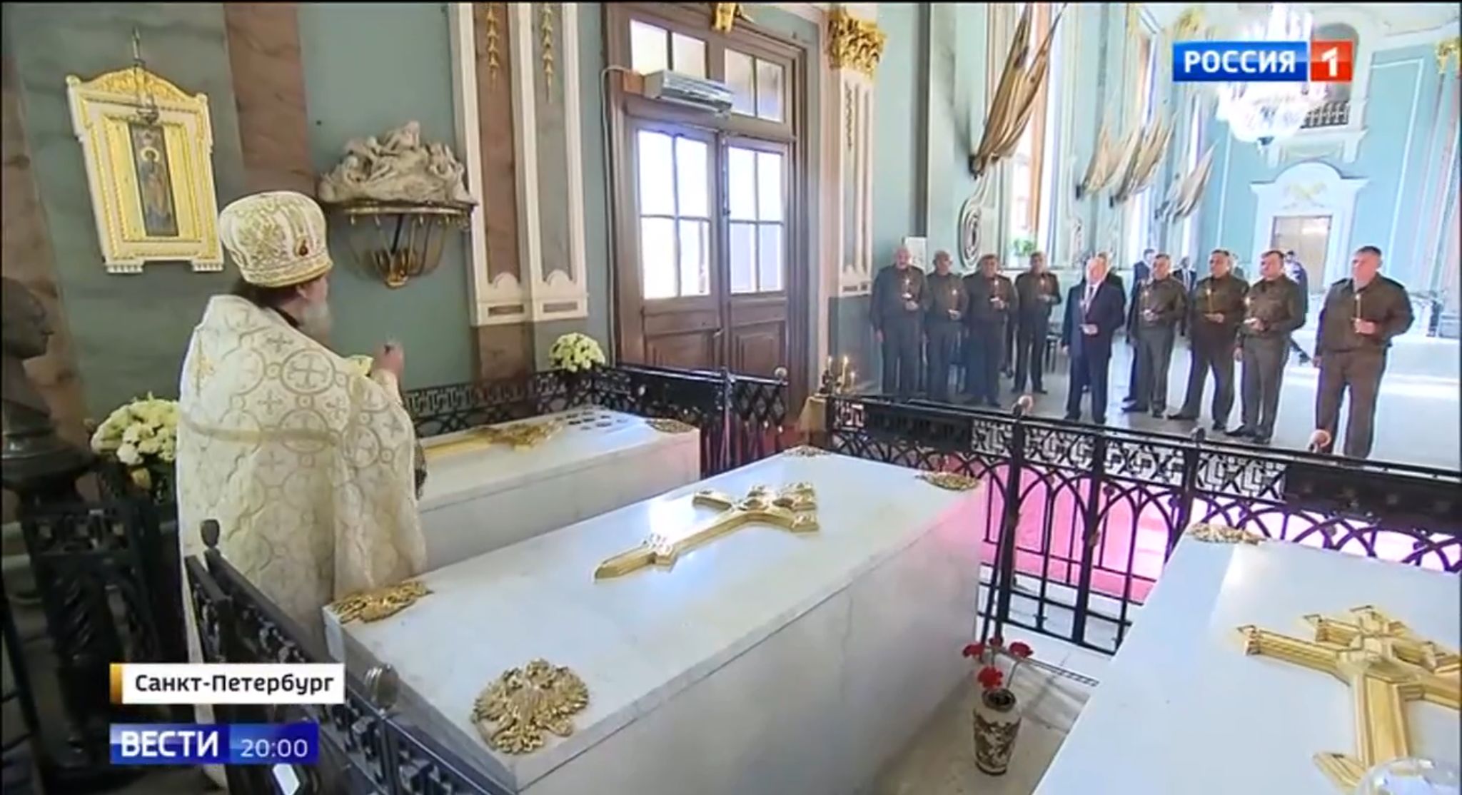Putin z wojskowymi stoją ze świeczkami. Na pierwszym planie pop pomiedzy dwomam marmurowymi grobowcami