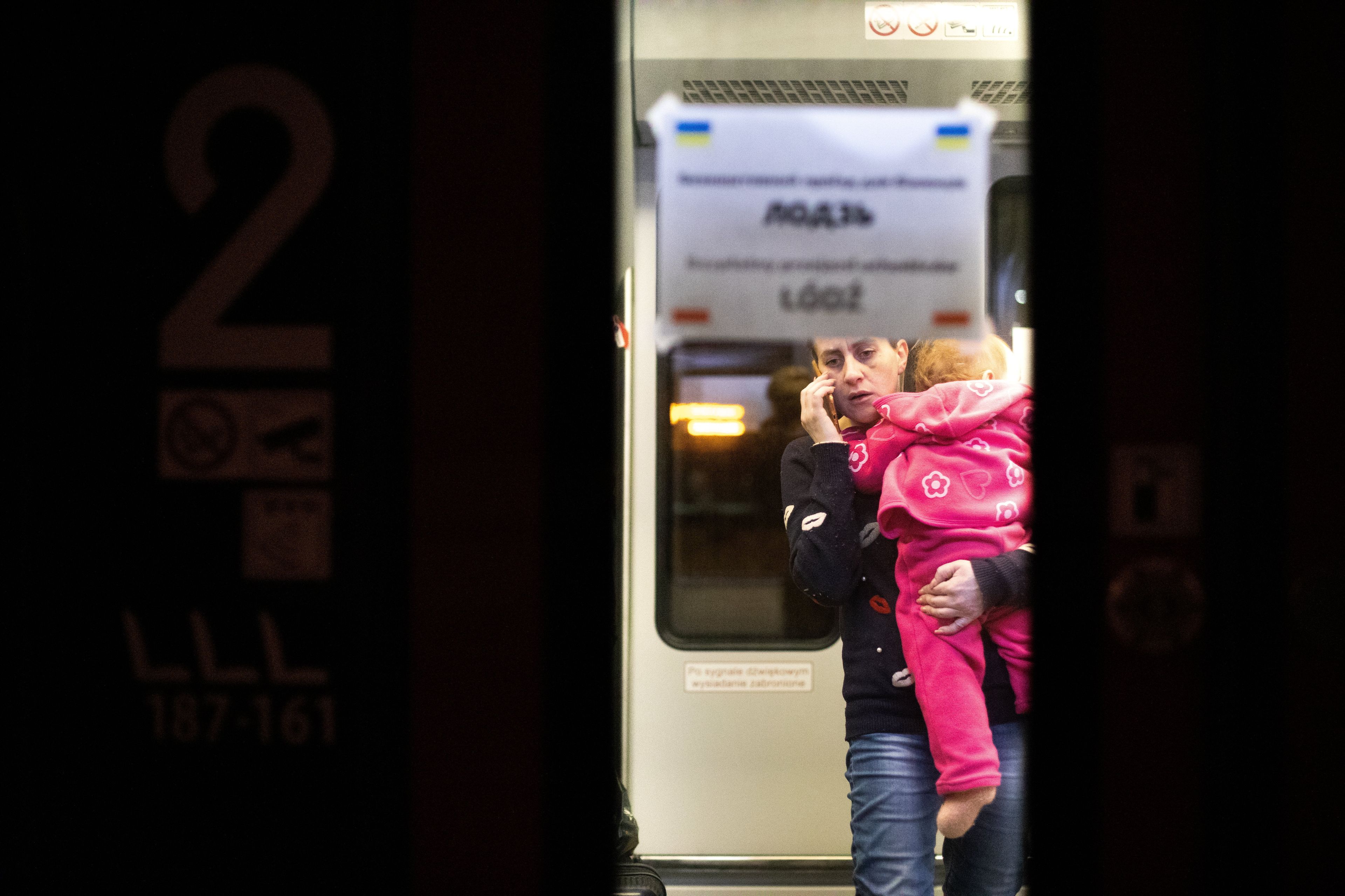 Na zdjęciu kobieta ok. 30 lat trzyma na rękach dziecko w różowym kombinezonie. Prawdopodobnie są w pociągu