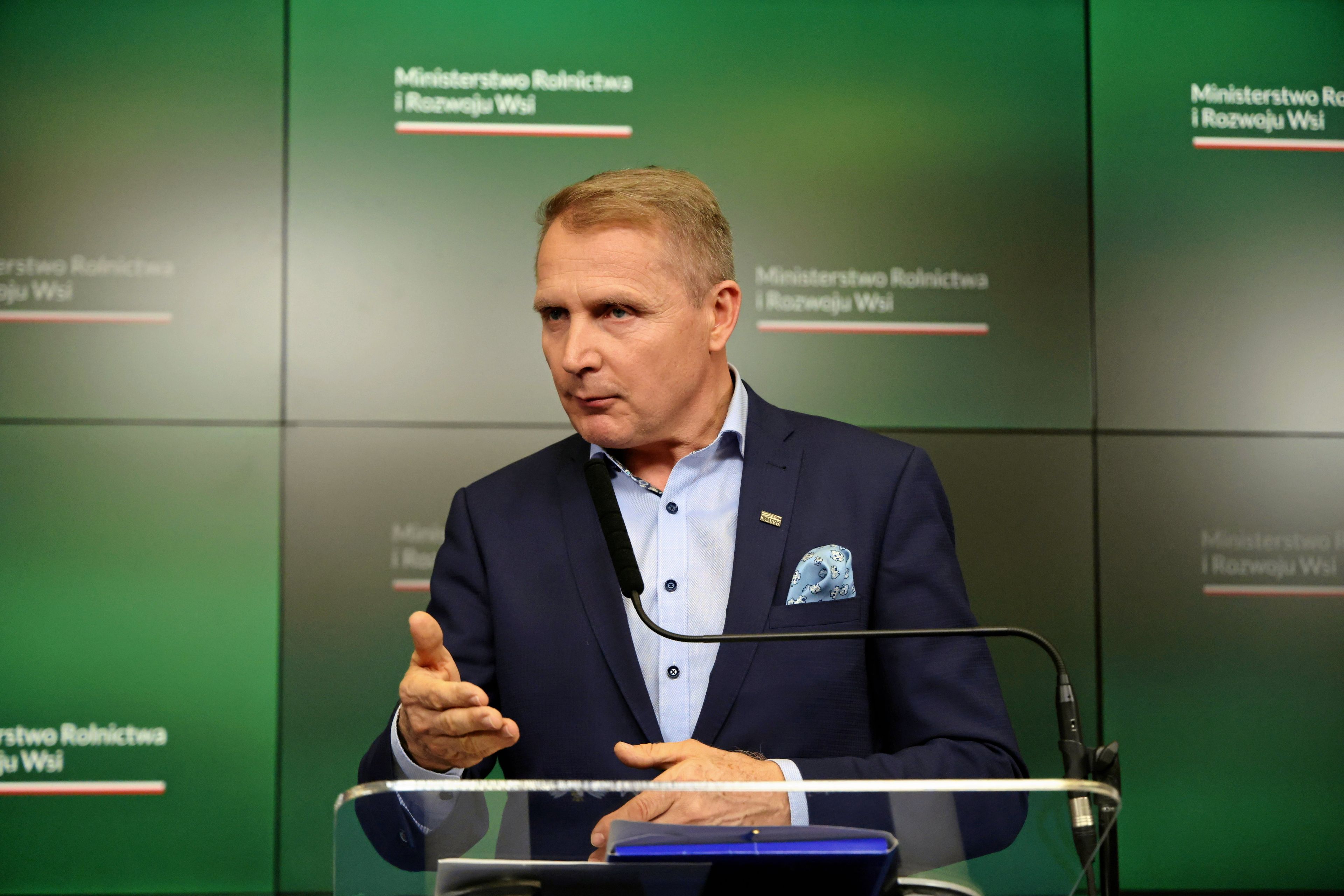 szef KOWR Henryk Smolarz w marynarce na tle zielonej planszy w czasie konferencji prasowej