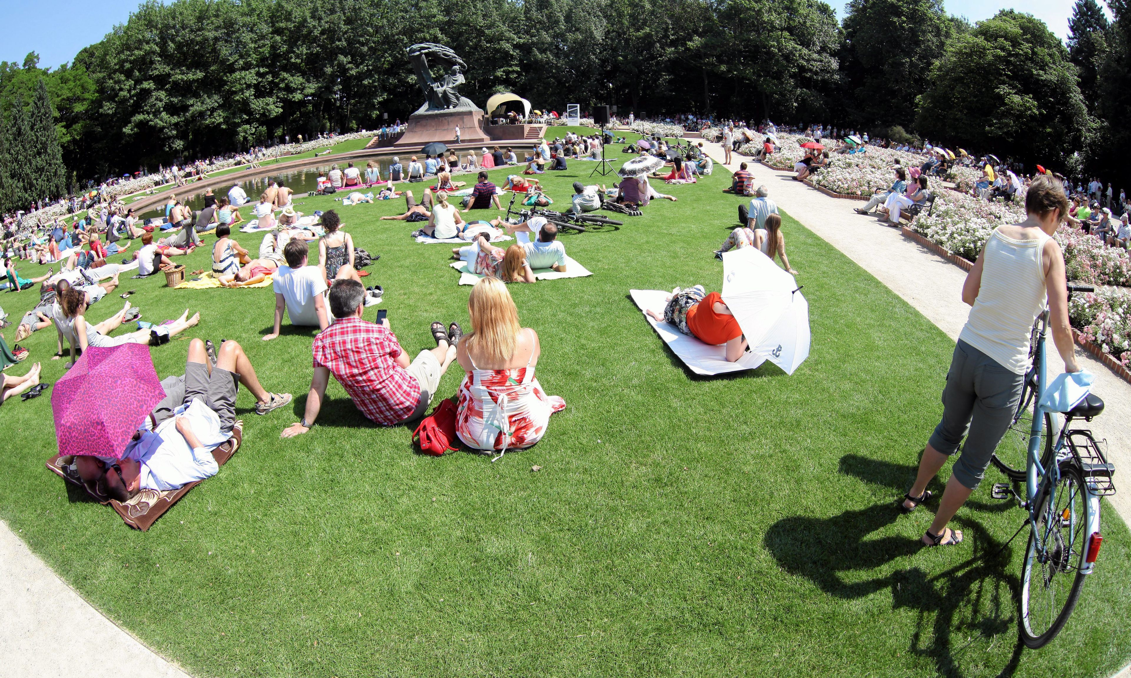 Ludzie siedzą na trawie i słuchają koncerytu pod pomnikiem Chopina w Warszawie