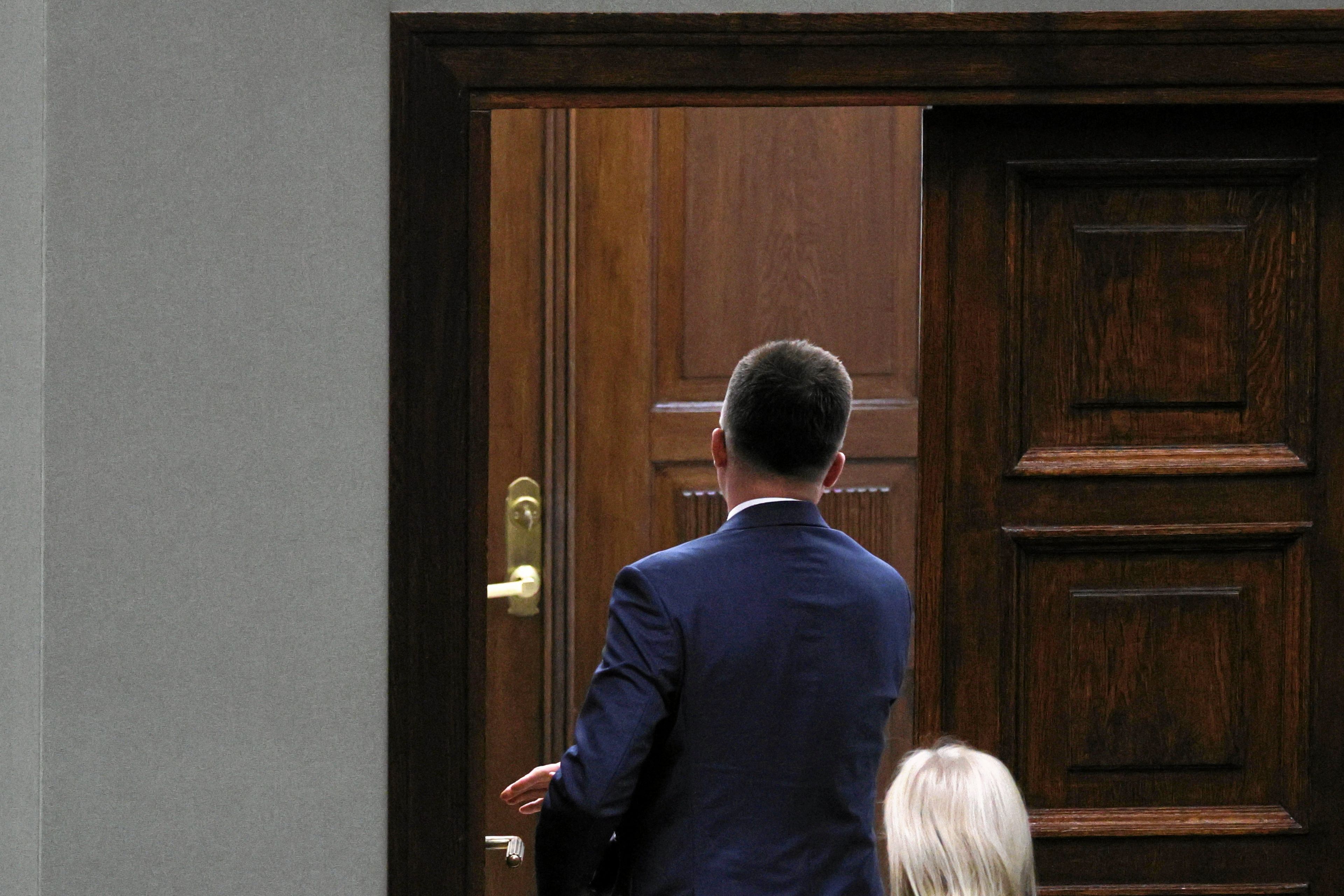 Sfotografowany od tyłu mężczyzna w garniturze wychodzi przez uchylone drzwi w Sejmie