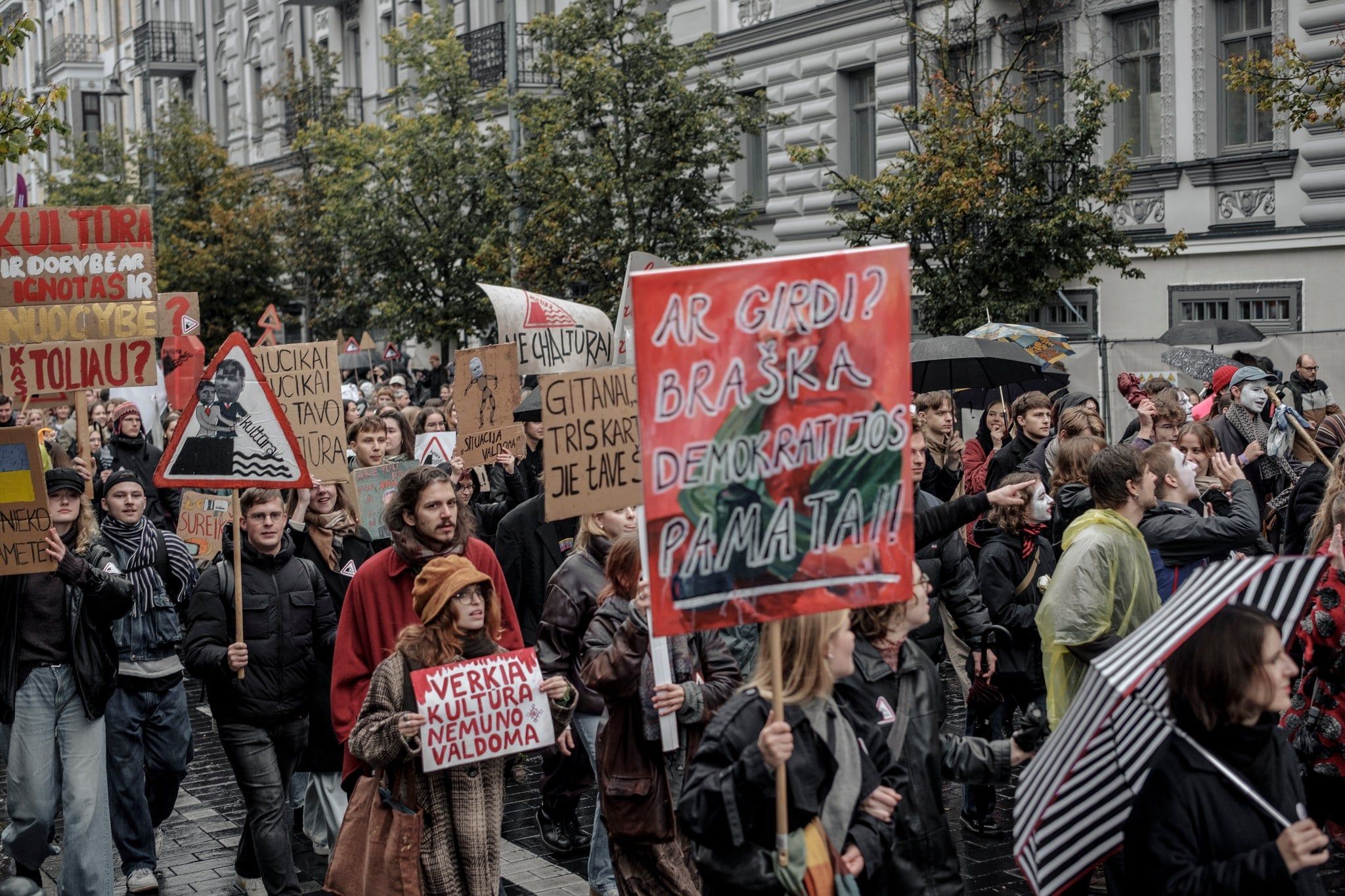 Deszczowy dzień, tłum ludzi idzie ulicą z kolorowymi banerami nad głowami