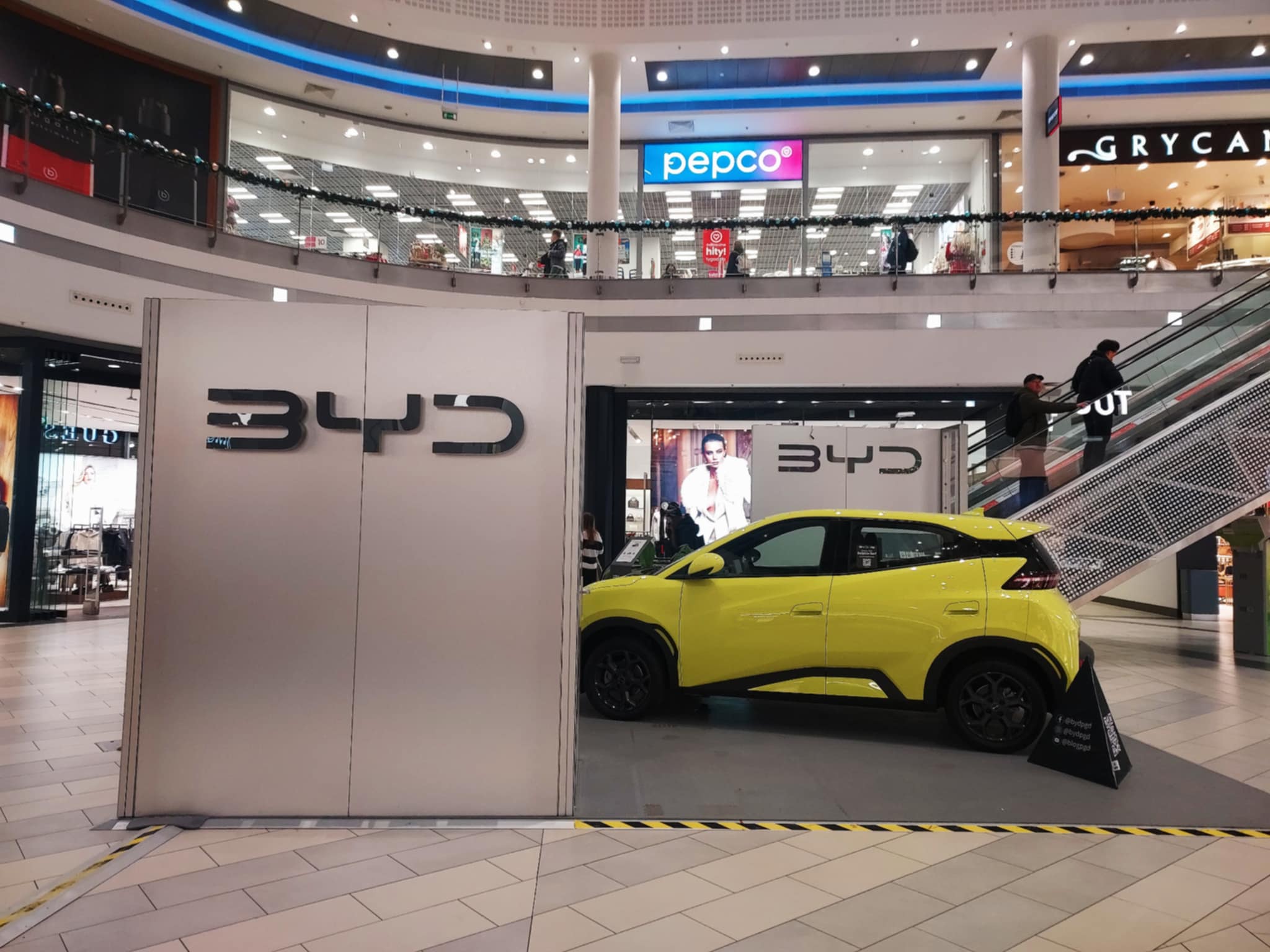 Limonkowy samochód elektryczny stoi na środku galerii handlowej. To reklama auta chińskiej marki BYD