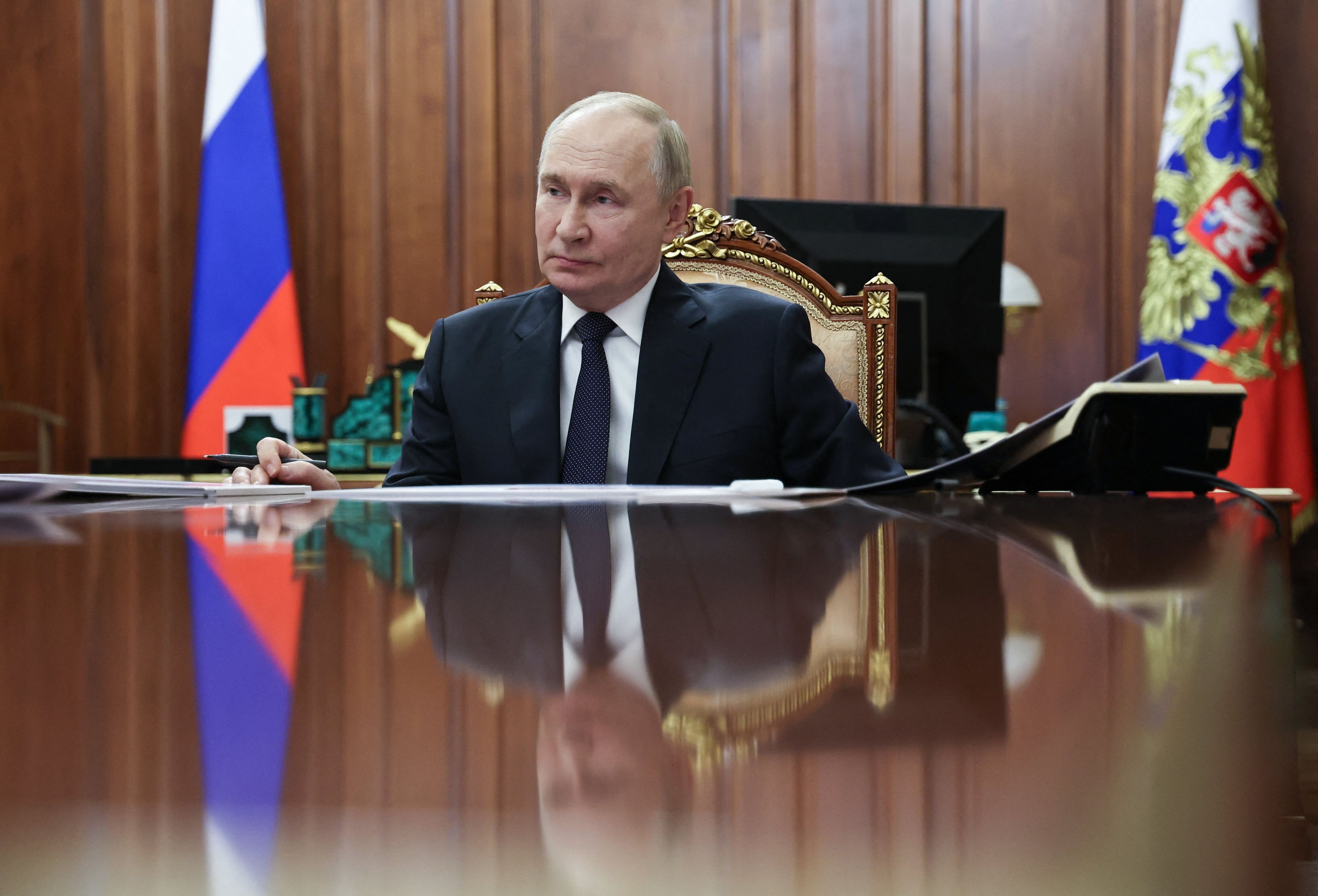 Putin przy biurku, w którym odbija się jego postać