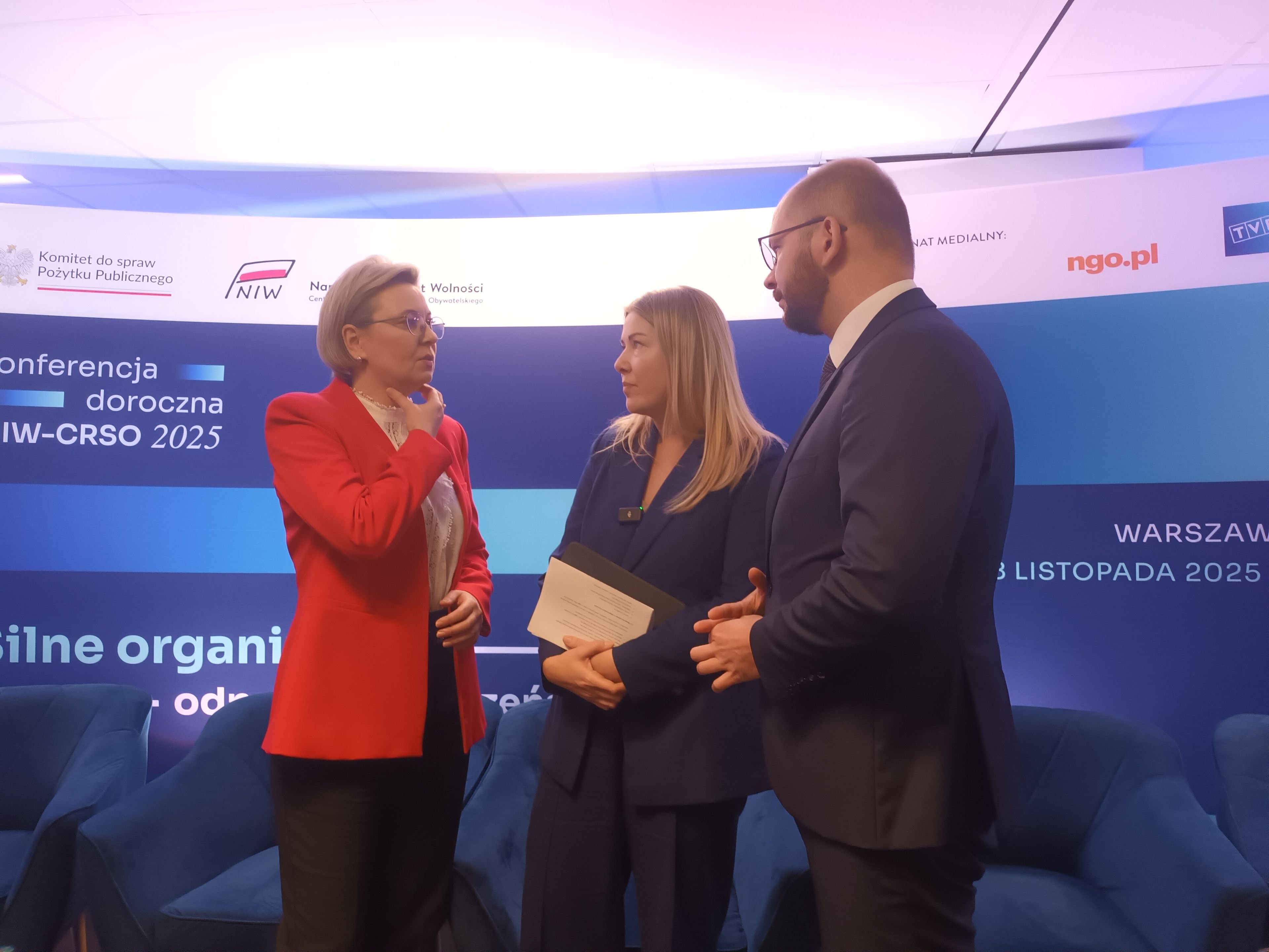 Konieta w czerwonej marynarce, kobieta w granatowej marynarce i męzczyzna w garniturze